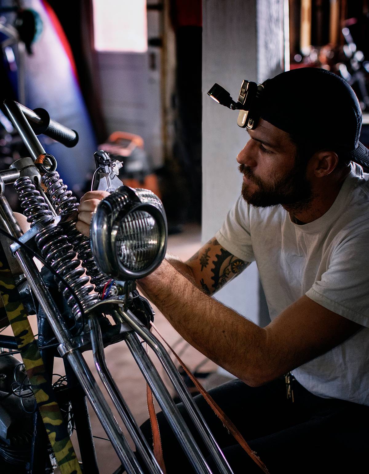 Een man met een hoofdlamp repareert een motorfiets in een werkplaats.