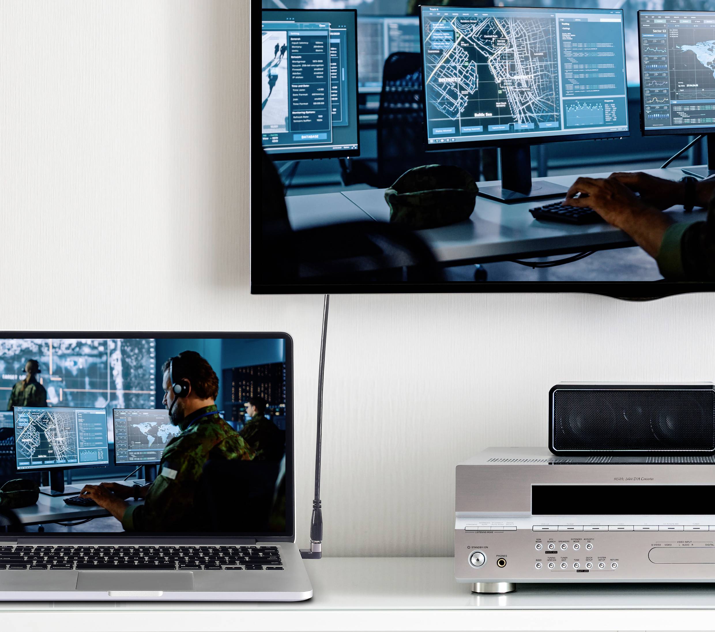 'Ruimte met monitors toont militaire kaarten en gegevens.' Een laptop weerspiegelt het hoofdscherm. Een versterker is onderaan geplaatst.