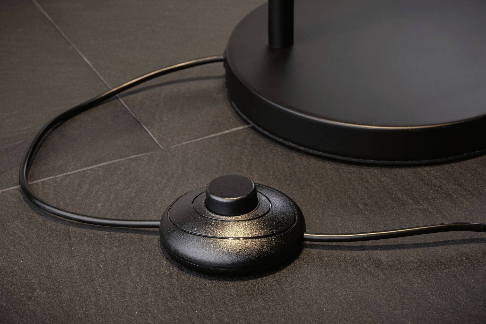 Zwarte voetschakelaar op een donkere ondergrond, verbonden met een kabel. De schakelaar bestuurt een elektrisch apparaat.