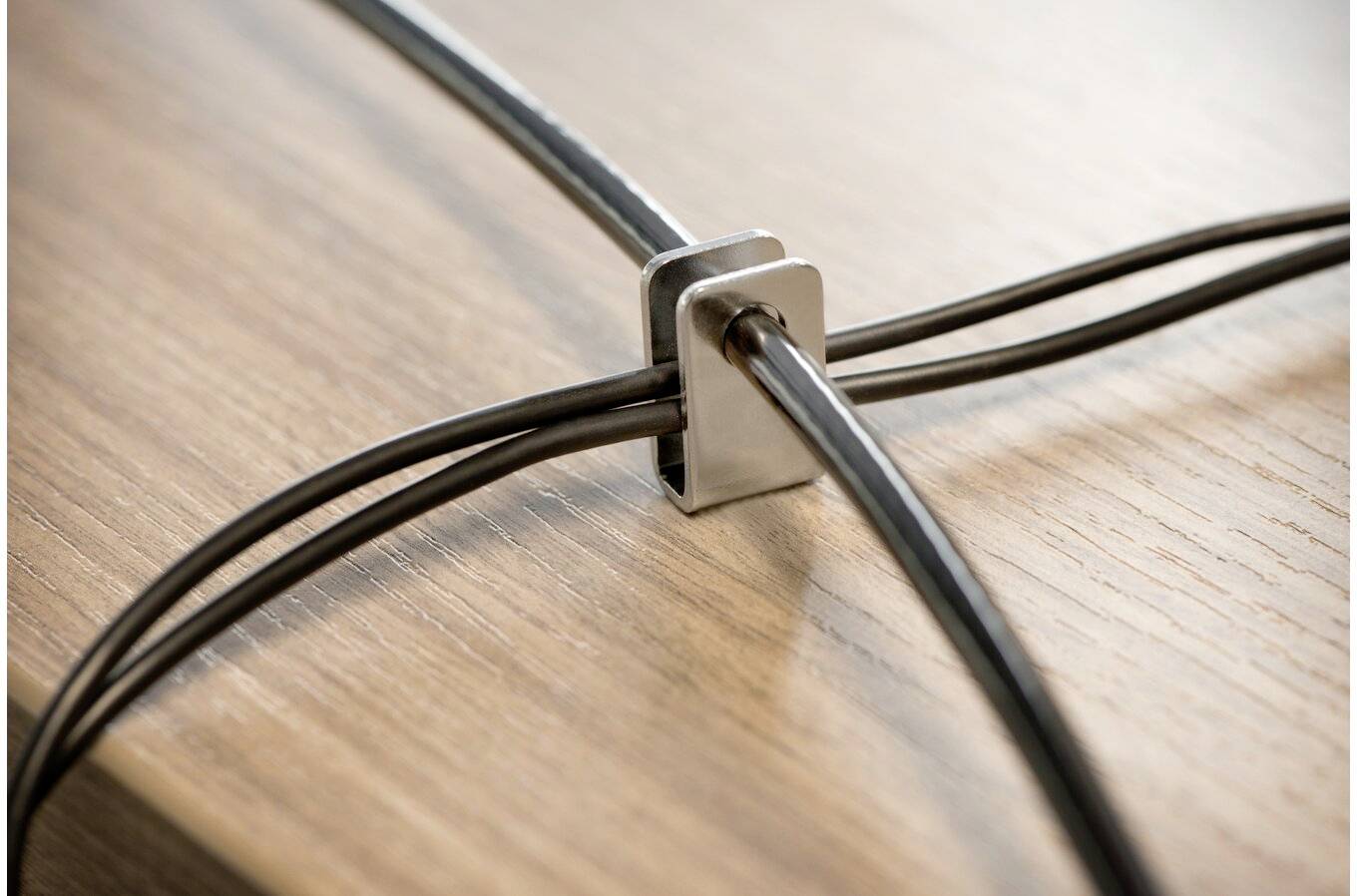Vier zwarte kabels worden bij elkaar gehouden door een metalen beugel op een houten ondergrond.