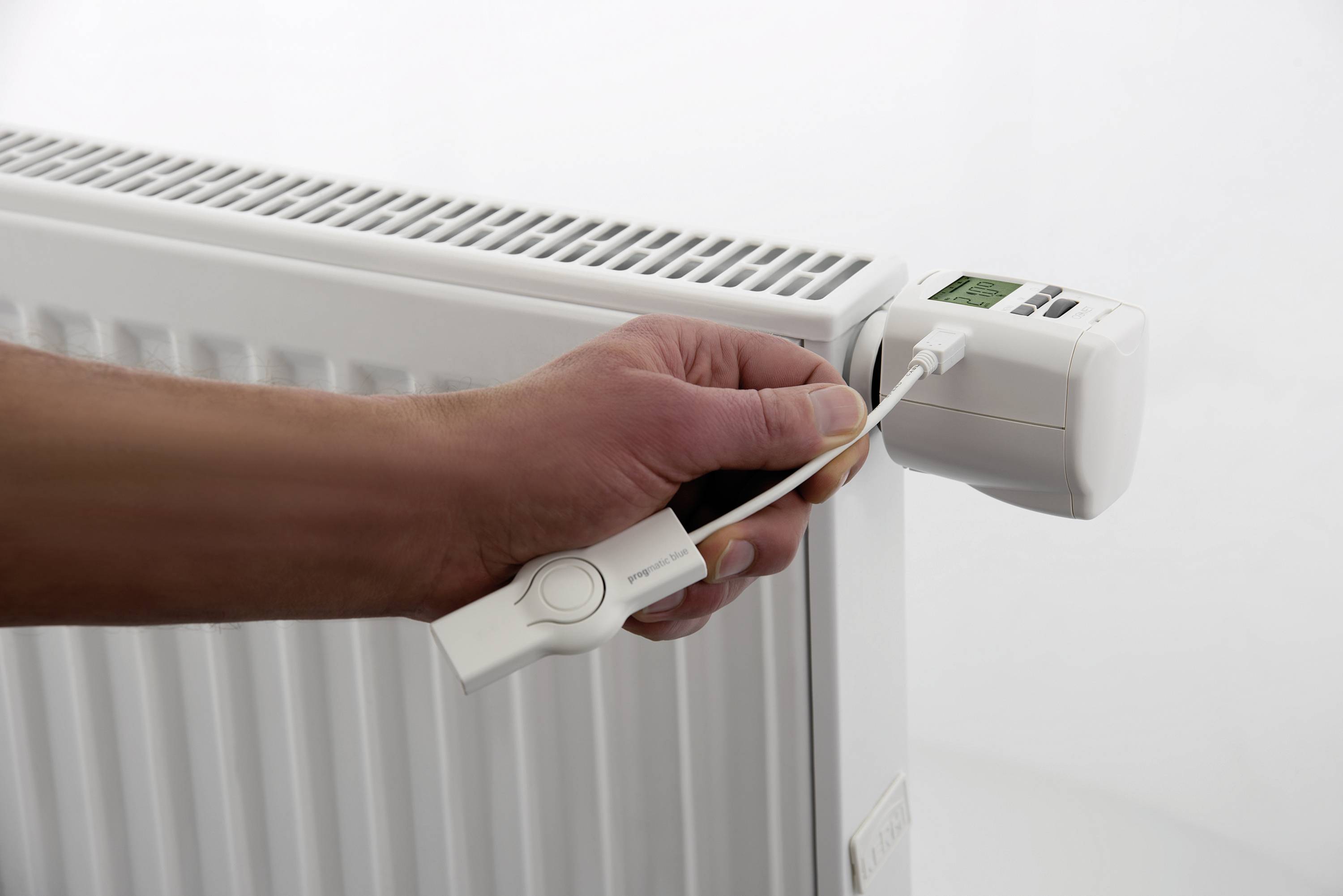 Een hand houdt een radiatorthermostaat vast met een instelgereedschap dat wordt aangebracht op een radiator.