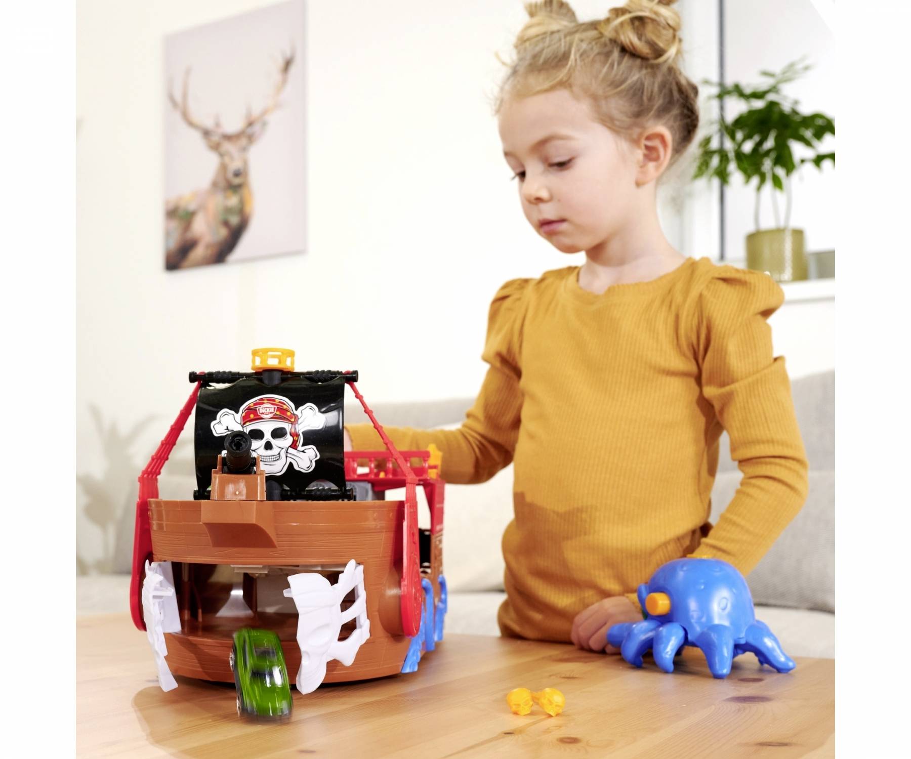 Een kind speelt met een piratenschip-speelgoed met een doodshoofd erop. Naast het schip ligt een blauwe octopus-pop op tafel.