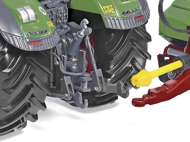 Een groene tractor met grote, zwarte banden wordt achteraan getoond. Een geel en rood aangehecht onderdeel is zichtbaar.