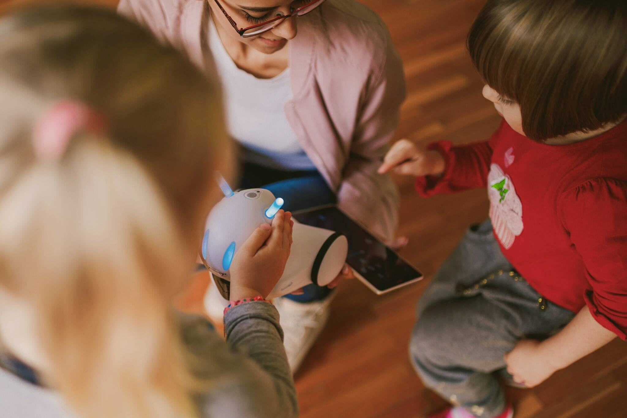 Een volwassene en twee kinderen interageren met een kleine robot die naar een tablet wijst.