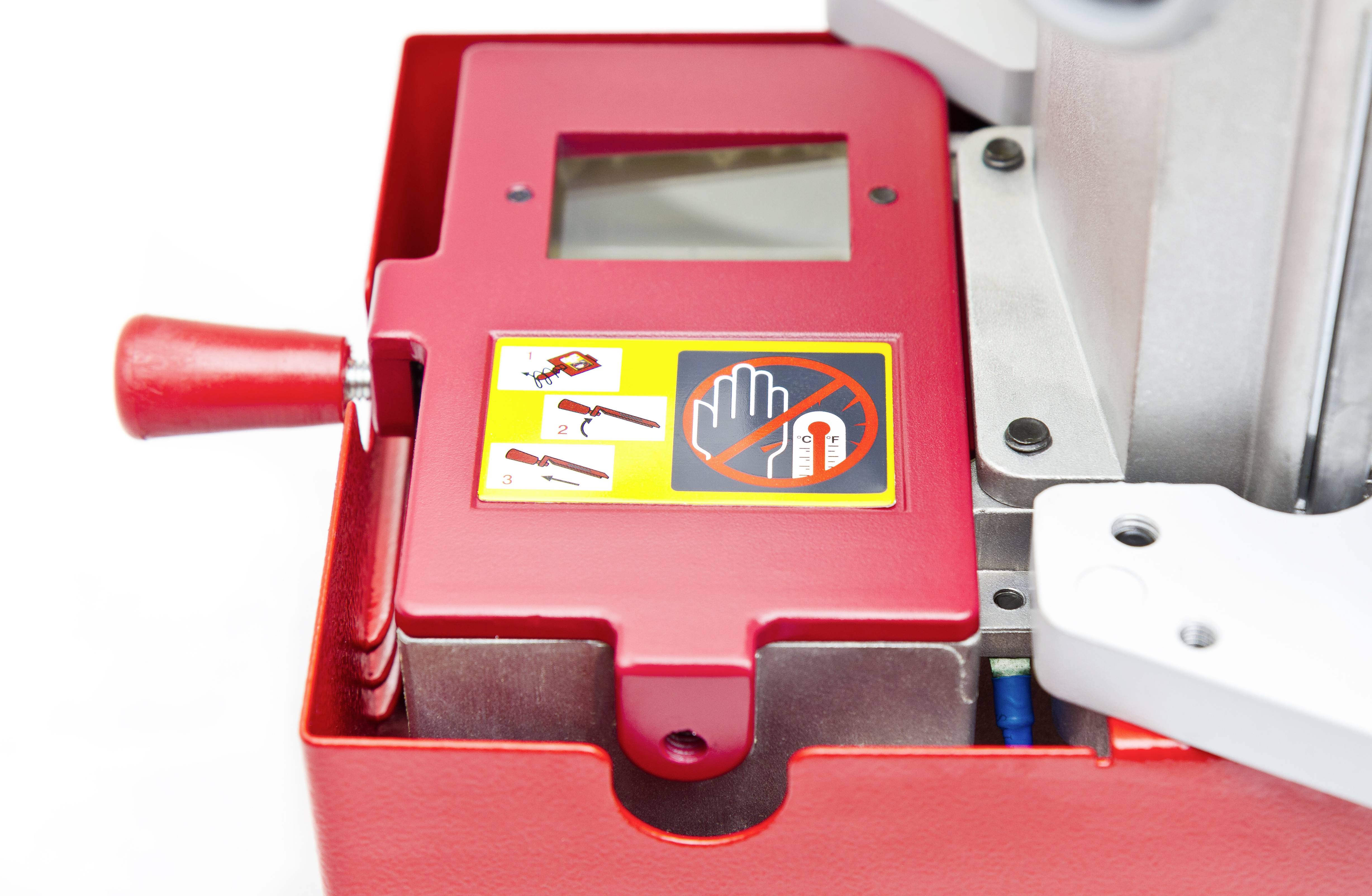 Rode machine met hendel en veiligheidswaarschuwing. Pictogrammen tonen waarschuwingen voor gebruik. Kijkvenster boven de hendel.