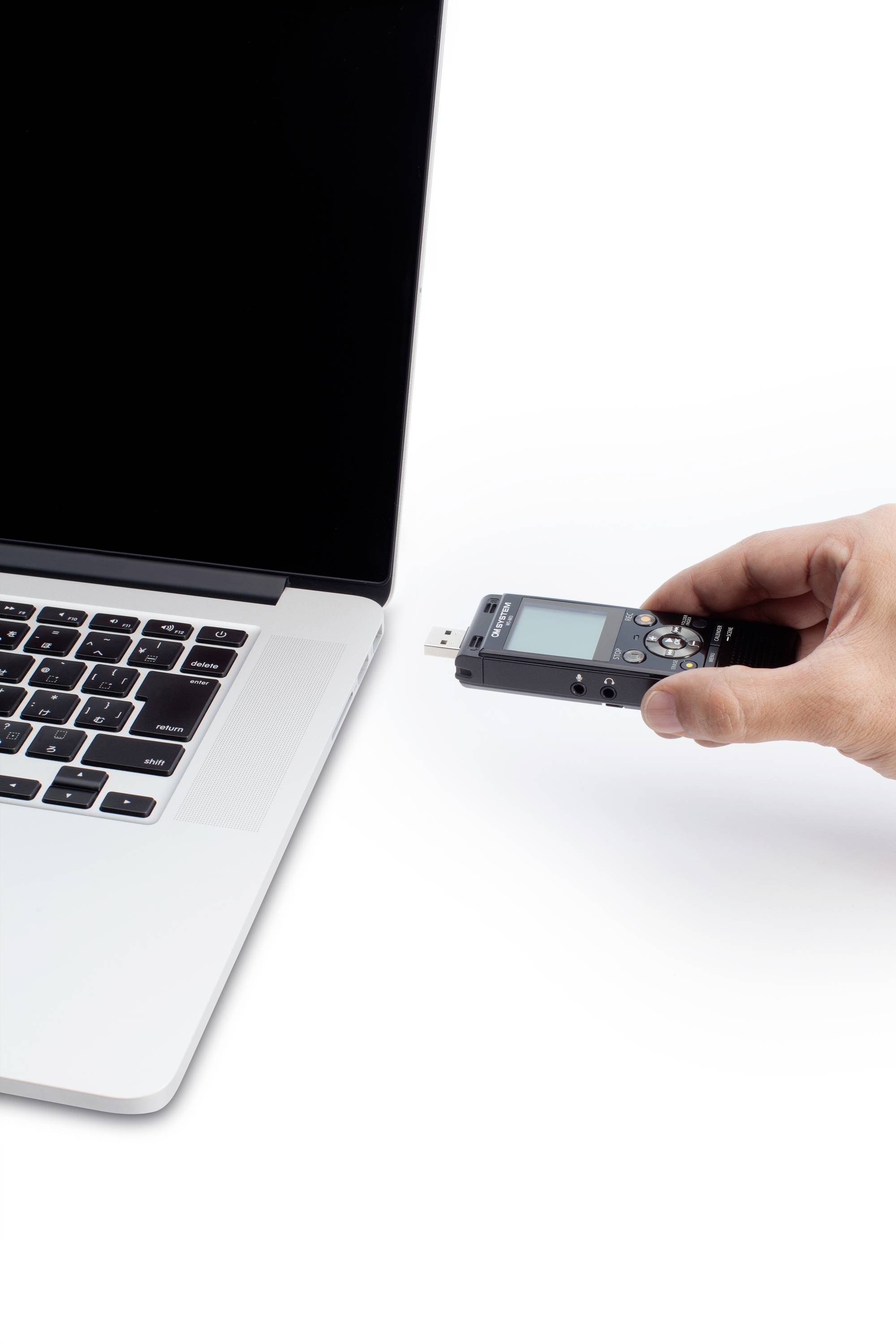 Een hand houdt een dictafoon vast die wordt aangesloten op een laptop. De laptop heeft een zwart scherm en een zilveren behuizing.