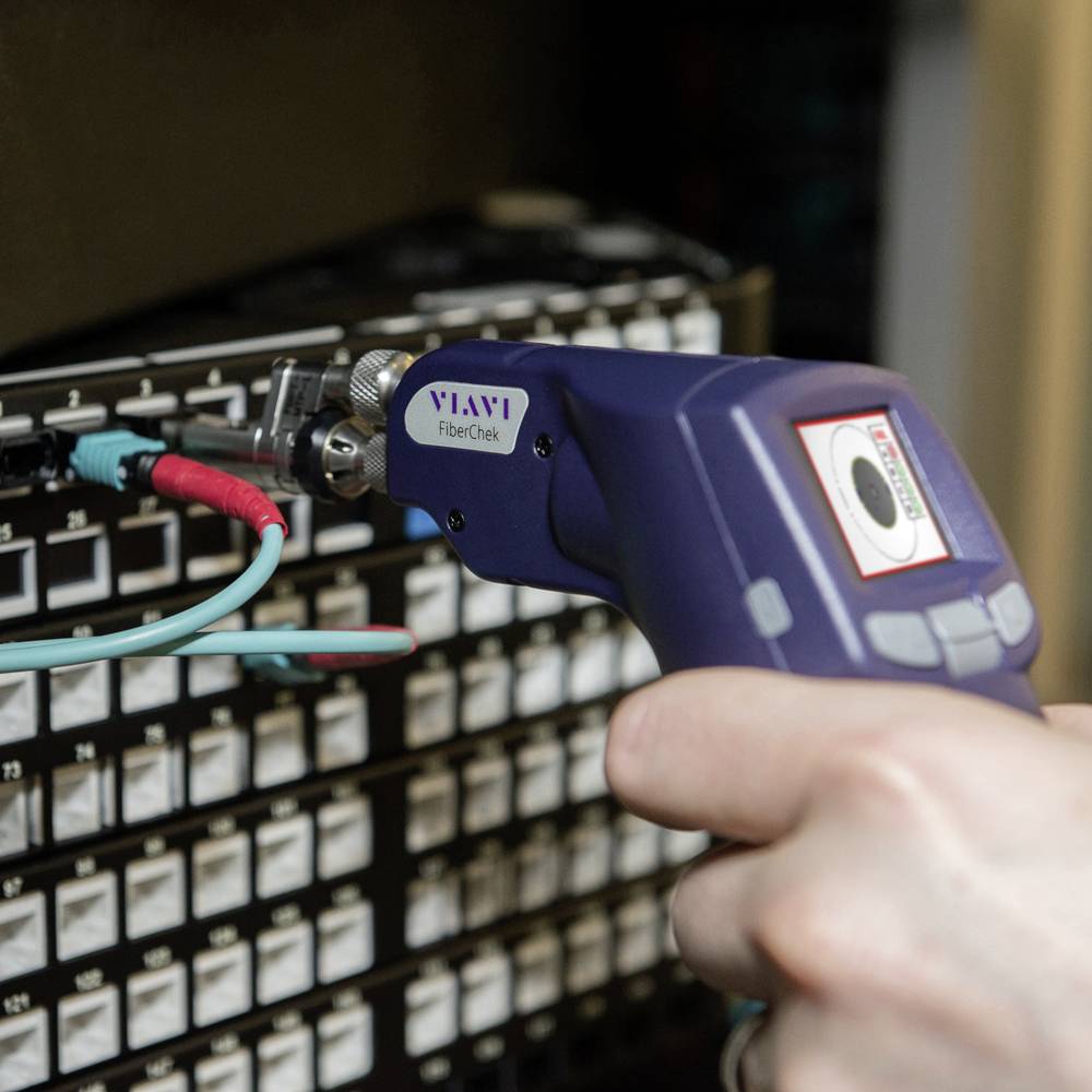 Een hand houdt een digitaal inspectie-microscoop vast om glasvezelverbindingen te controleren op een netwerkkabel patchpanel.