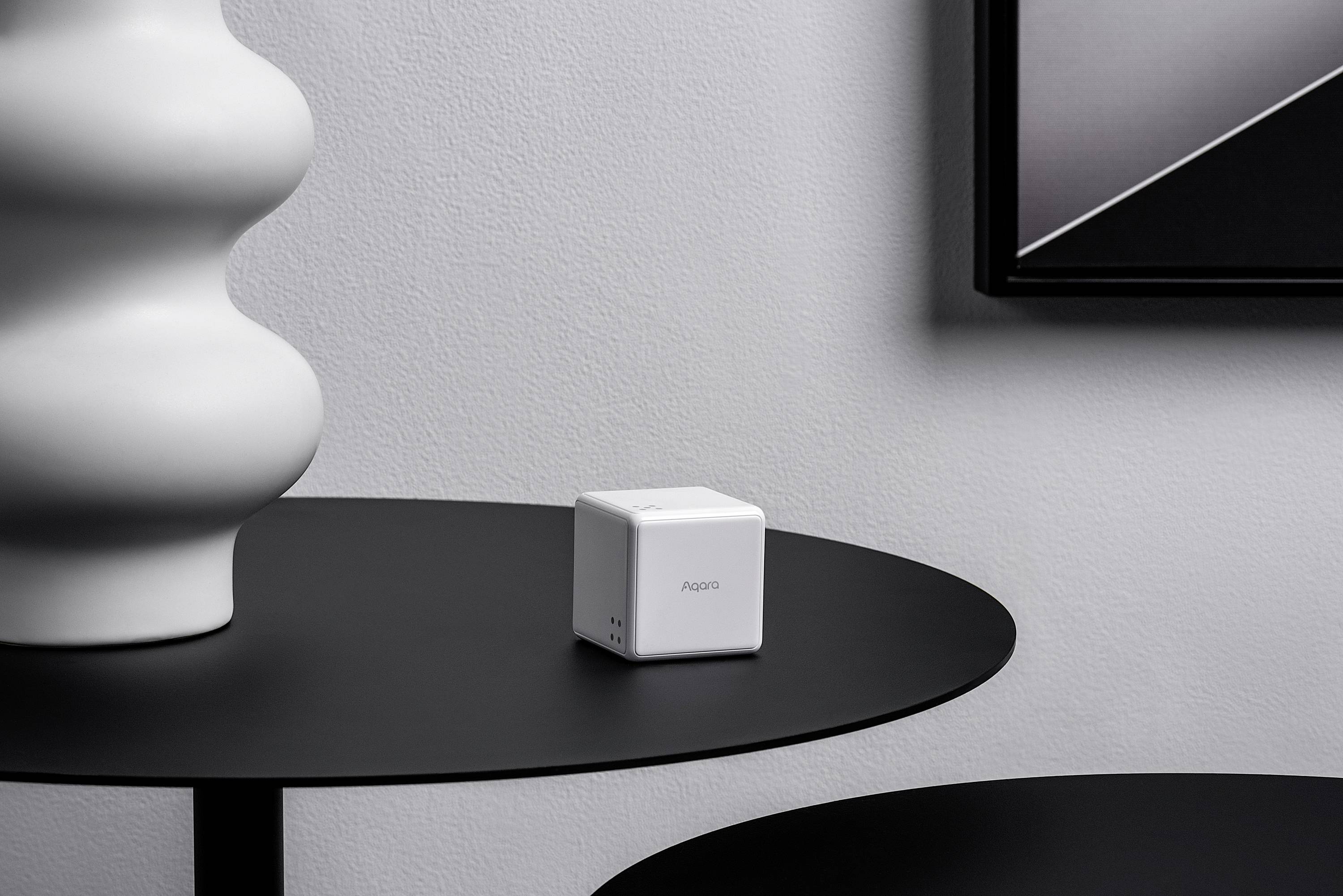 Een witte kubus met de tekst 'HD03' staat op een rond, zwart tafeltje in een minimalistische ruimte.