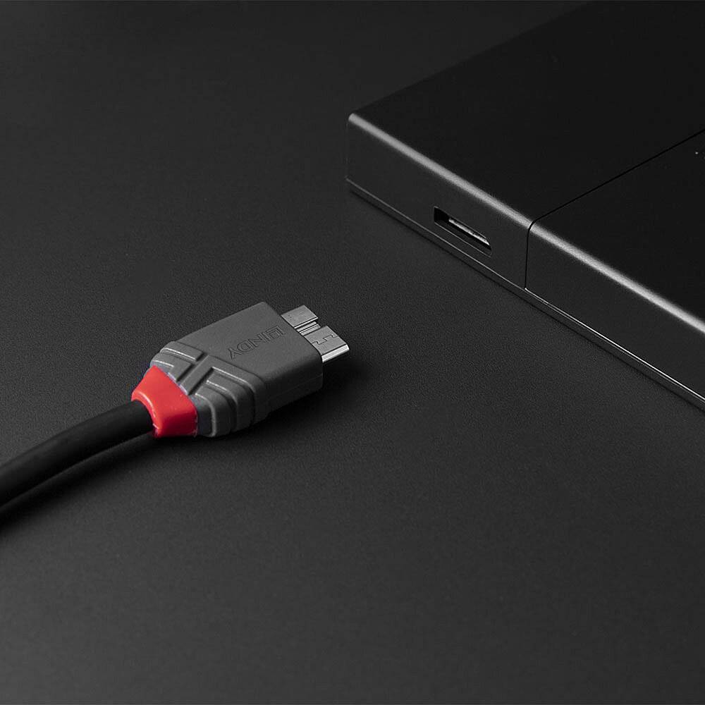 Een HDMI-kabel met een grijze stekker en rode details ligt dicht bij een zwart elektronisch apparaat op een donker oppervlak.