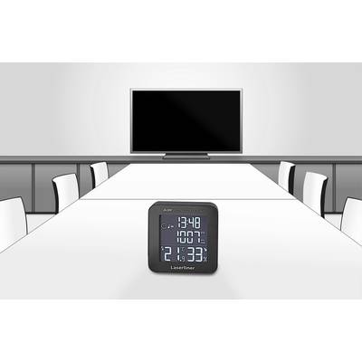 Een kleine, digitale hygrometer toont de tijd, temperatuur en luchtvochtigheid in een moderne vergaderruimte met tafel en stoelen.
