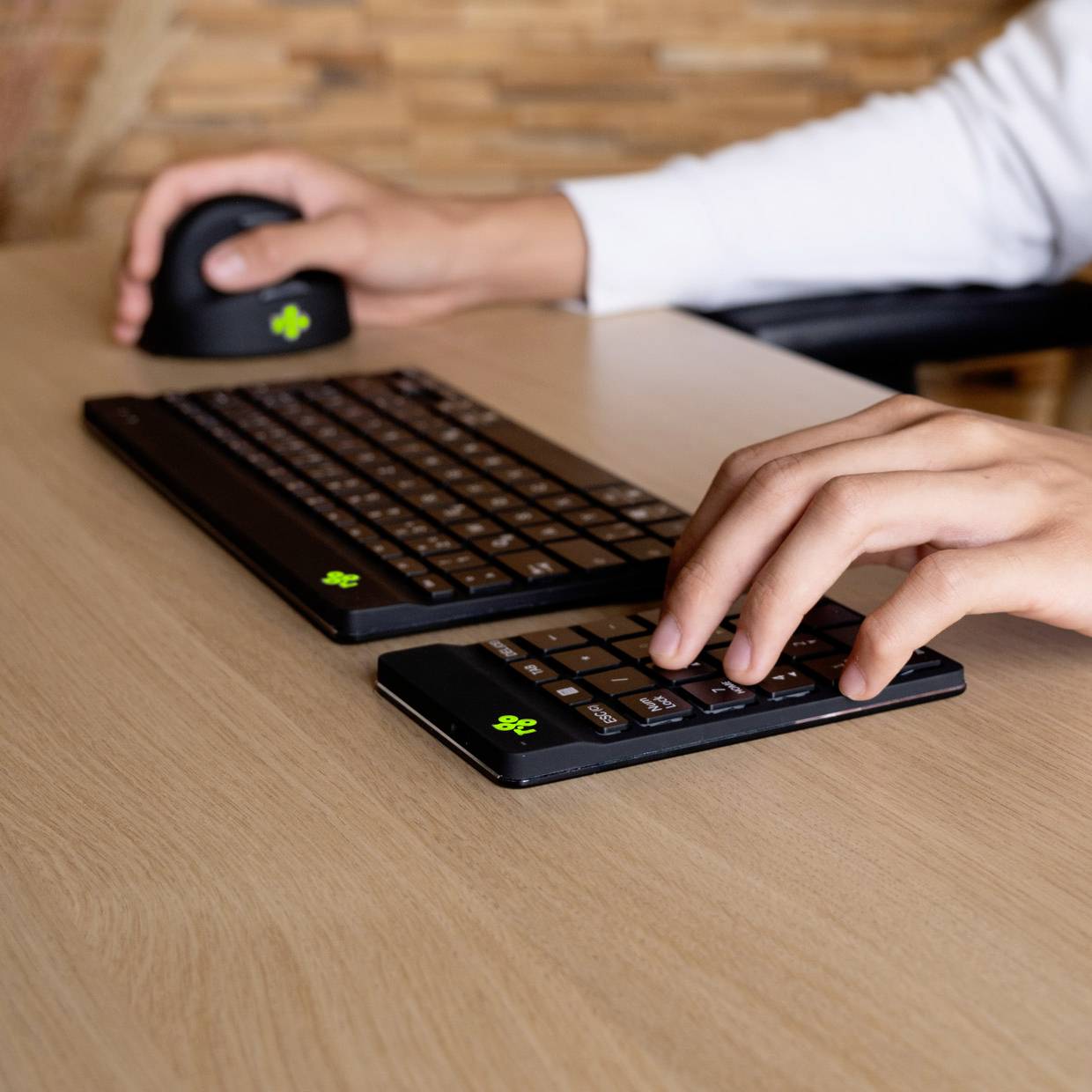 Een persoon werkt aan een tafel met een toetsenbord, een muis en een smartphone. De persoon typt op een numeriek toetsenblok.