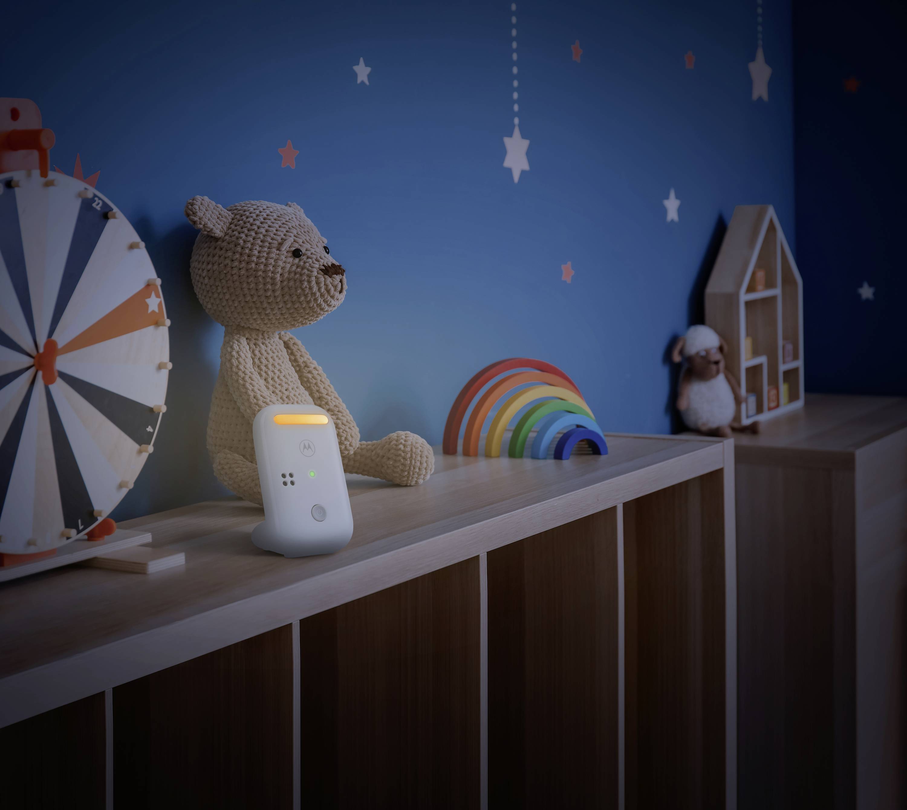 Een kinderkamer met een knuffelbeer en een nachtlampje op een plank. De blauwe achtergrond heeft sterren als decoratie.