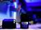 Een 12V Dremel lithium-ion accu en een oplader op een tafel in een werkplaatsomgeving met blauwe verlichting.