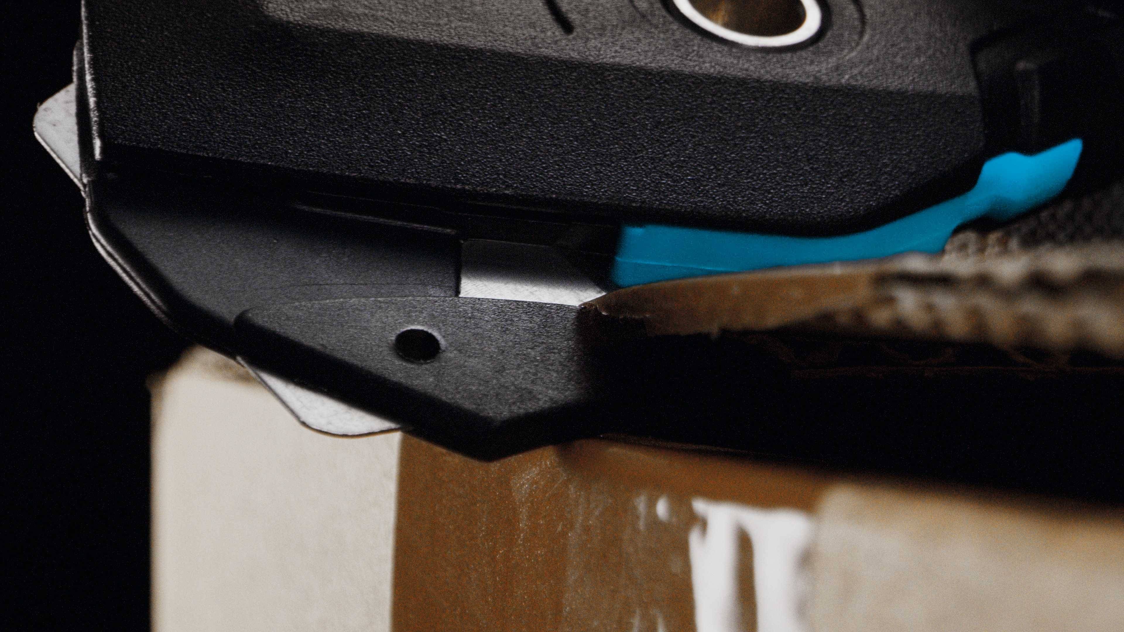Een close-up toont een scherp mes dat karton doorsnijdt. De afbeelding benadrukt de precisie en scherpte van het gereedschap.