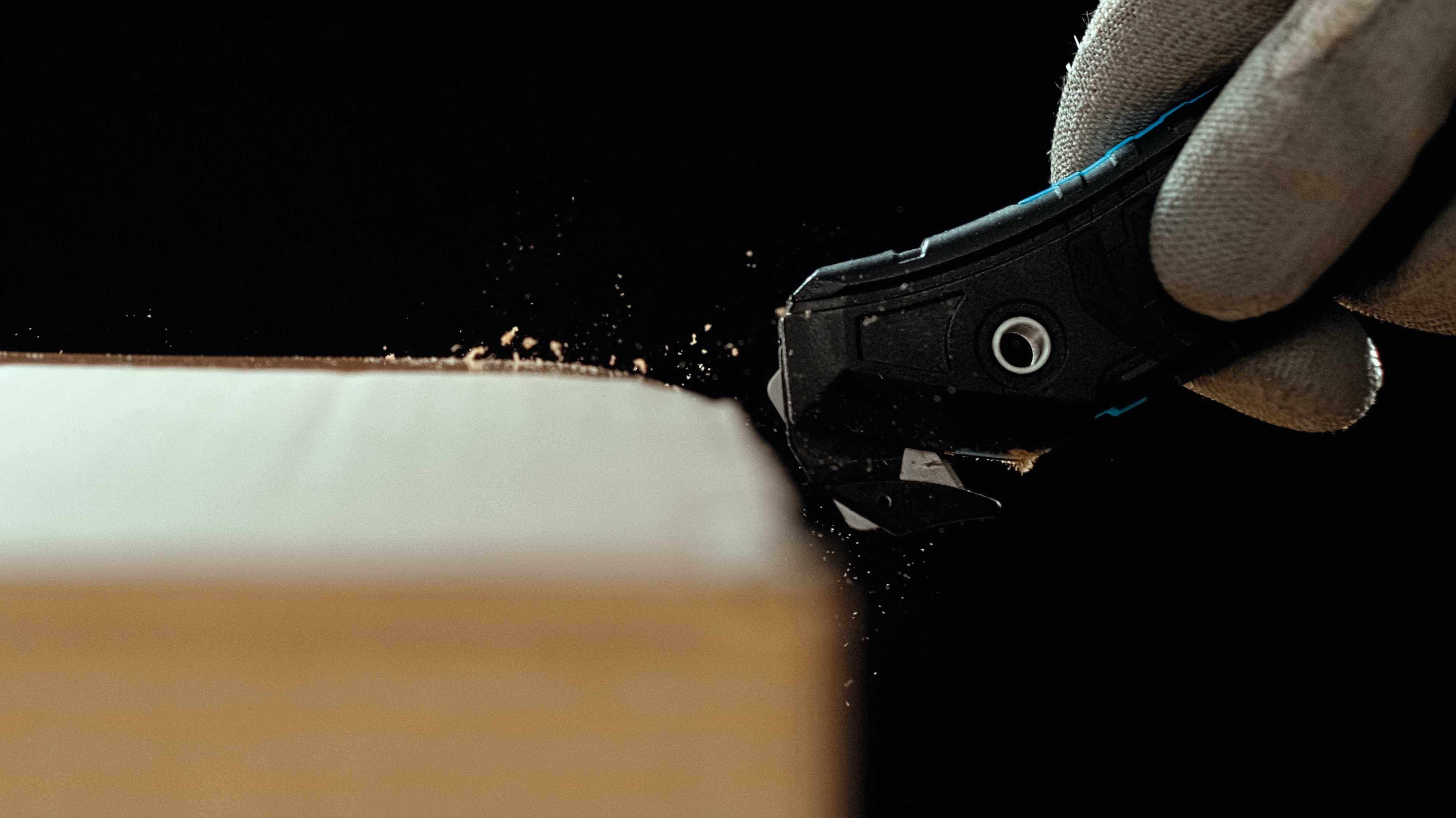 Een hand met handschoen snijdt hout met een cuttermes.