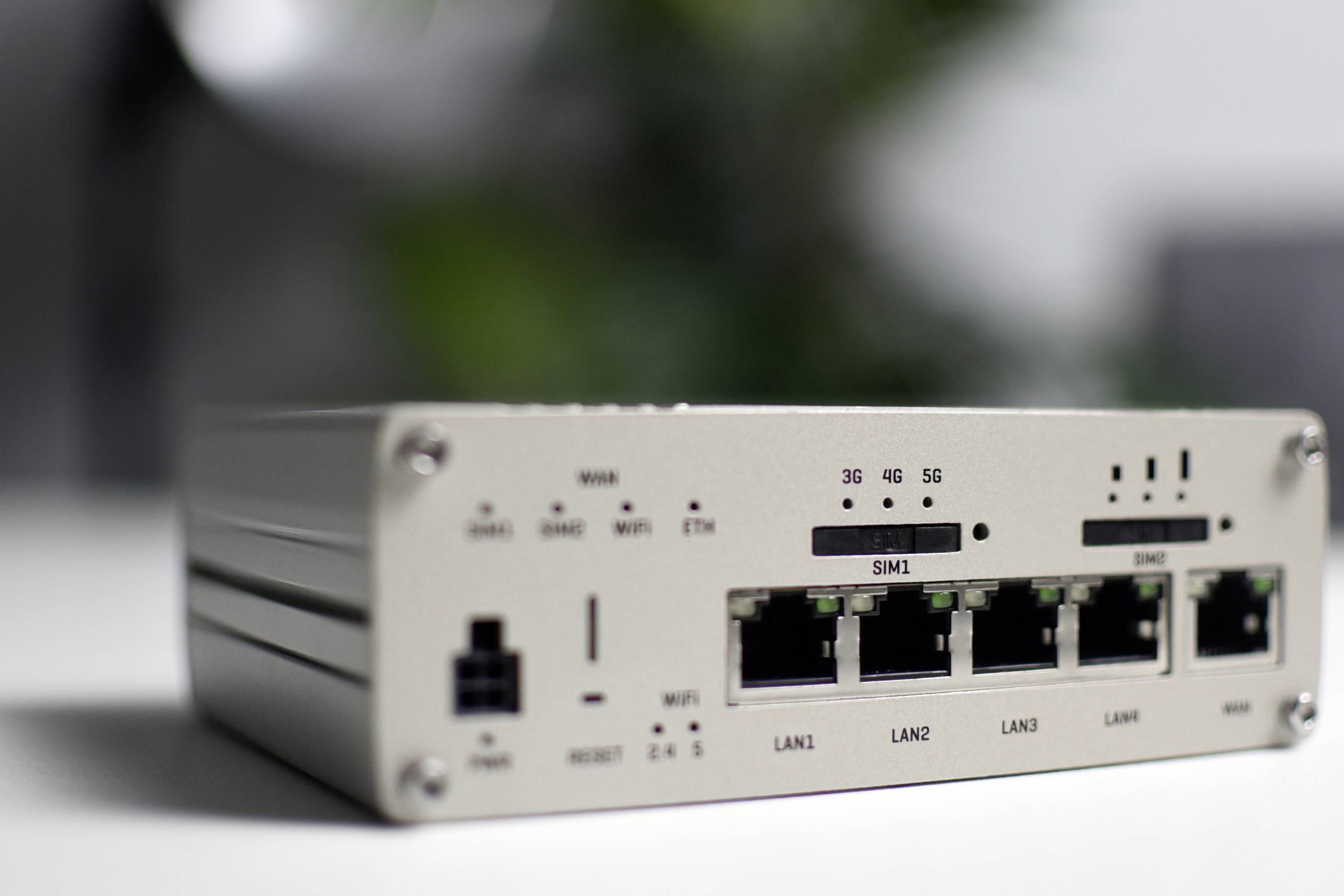Een zilveren router met vier Ethernet-poorten en SIM-kaartsleuven voor 3G/4G/5G-verbindingen, geplaatst op een bureau.
