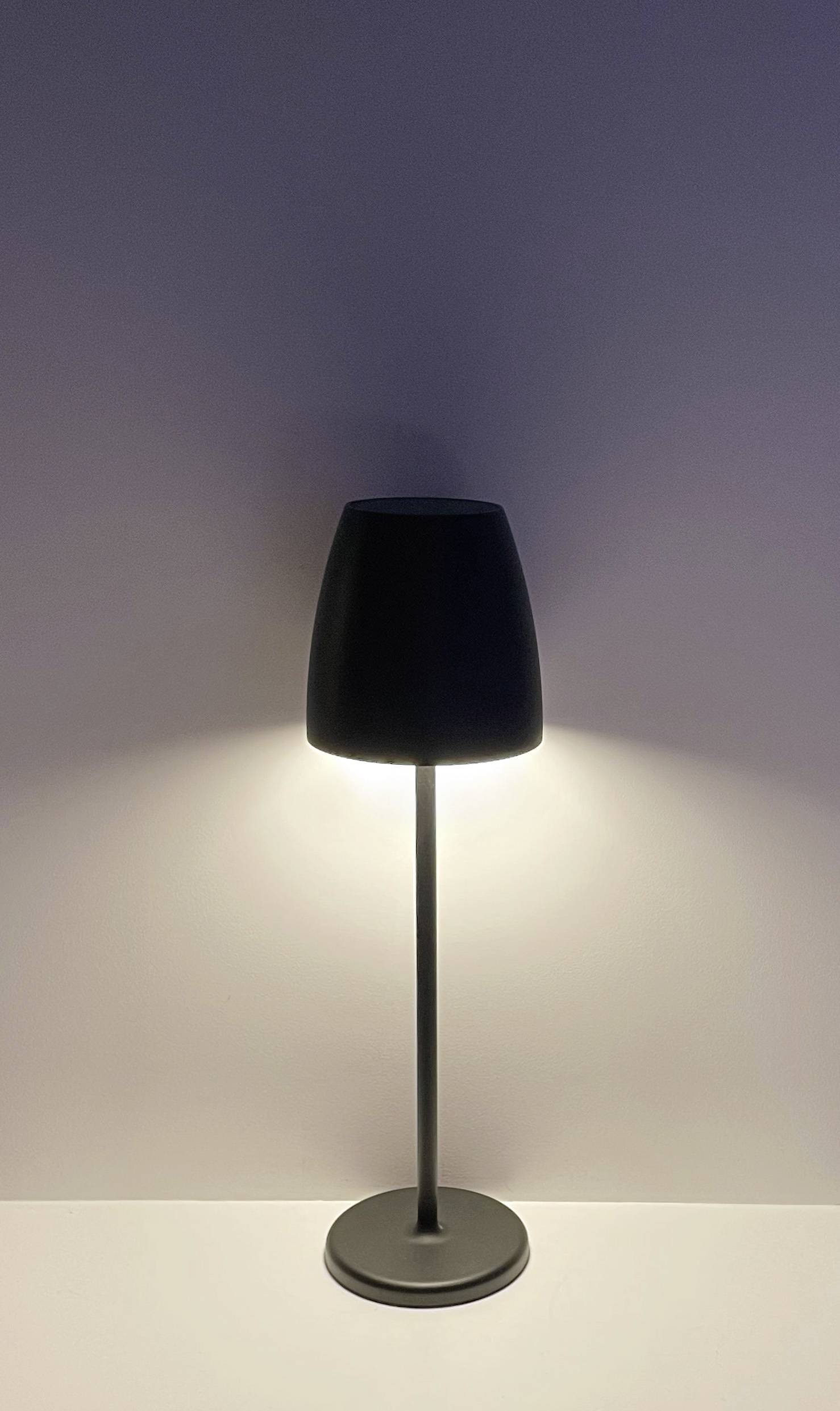 Een zwarte staande lamp schijnt tegen een witte muur. Het licht straalt naar boven en beneden, zorgt voor een zachte verlichting.