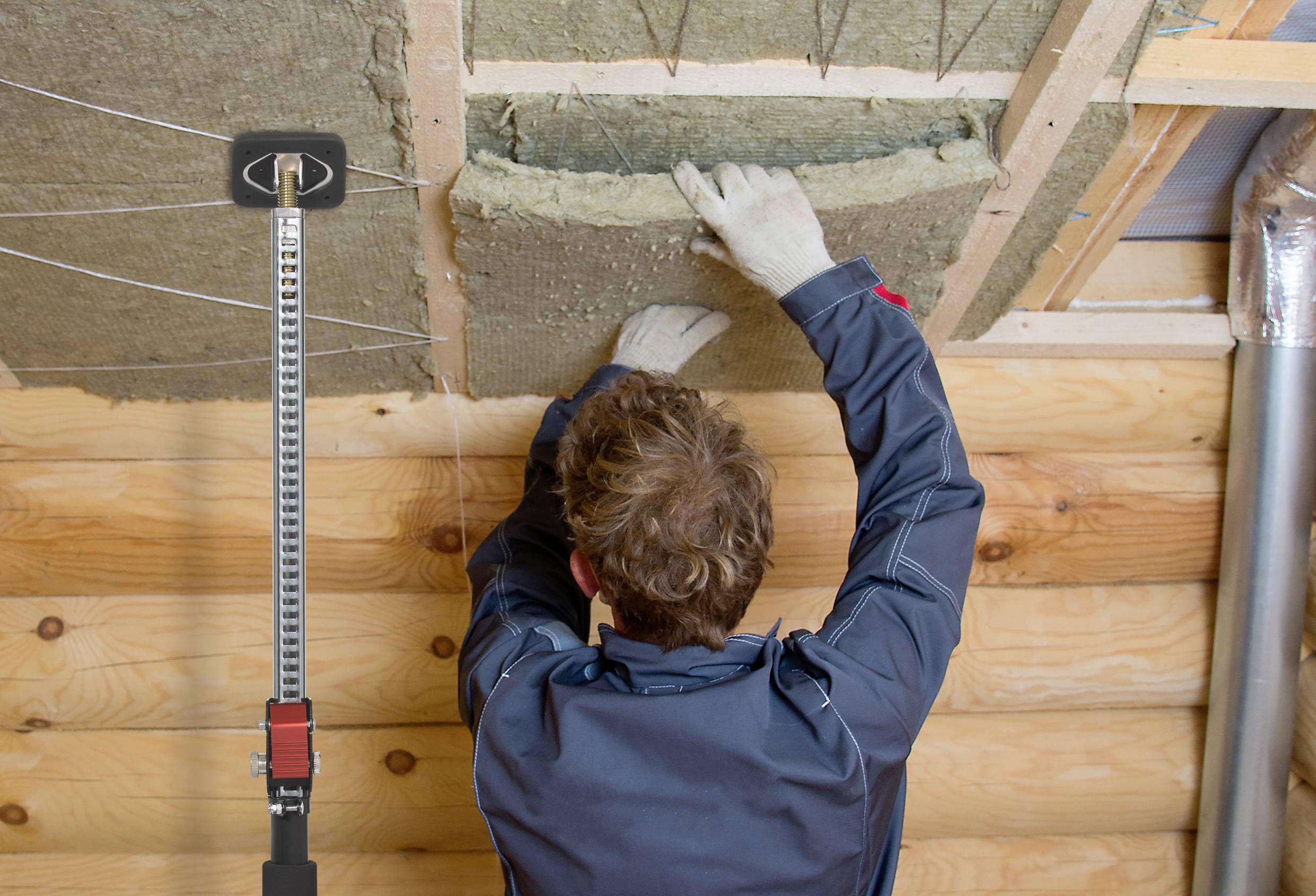 Een persoon brengt isolatiemateriaal aan aan een houten plafond in een gebouw. Terloops is een steun zichtbaar voor ondersteuning.
