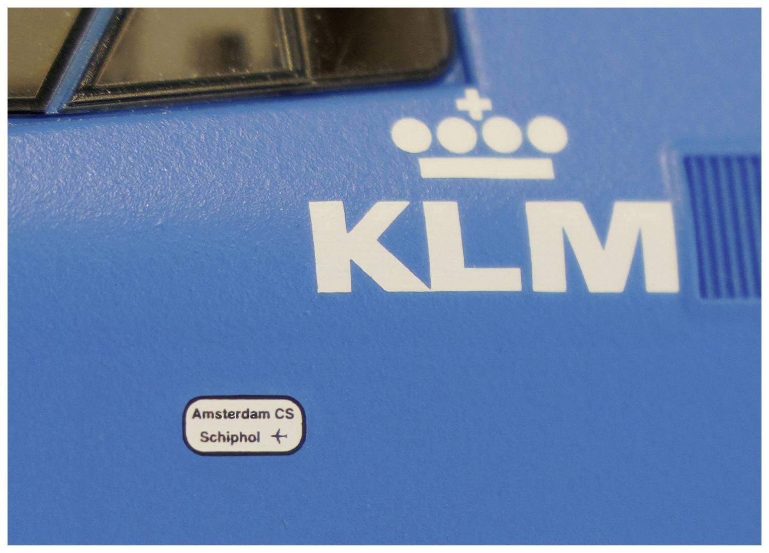 Blauwe trein met KLM-logo, met suggestieve lijnen van het Nederlandse spoorwegnetwerk, waaronder 'Amsterdam CS' en 'Schiphol'.