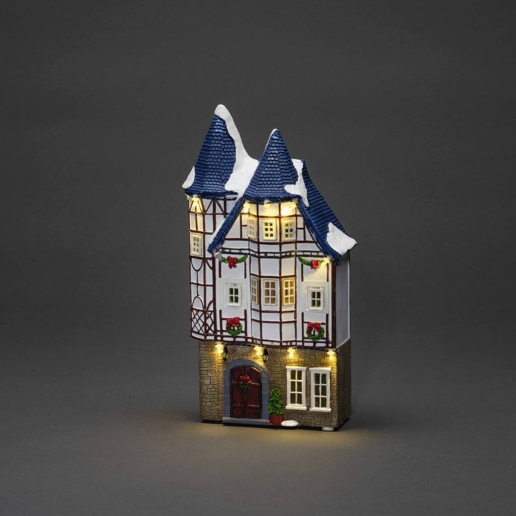 Een miniatuurmodel van een vakwerkhuisje met blauw-witte puntdaken en verlichte ramen, op een grijze achtergrond.