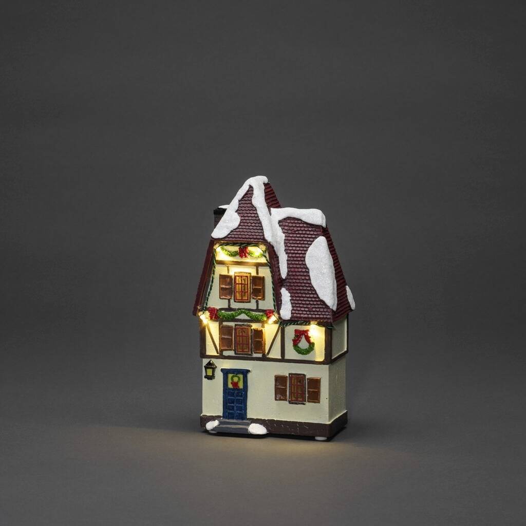 Verlicht miniatuurbuis bedekt met sneeuw op het dak en de ramen, versierd met een kerstkrans, op een grijze achtergrond.