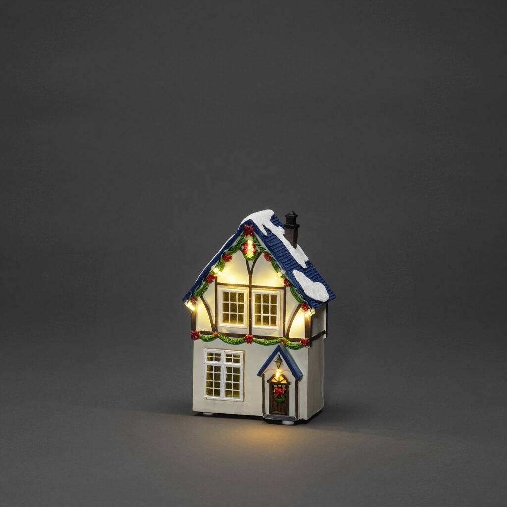 Een klein modelhuis met kerstdecoratie en lichtjes, dat staat op een grijze achtergrond. Het dak is bedekt met kunstsneeuw.