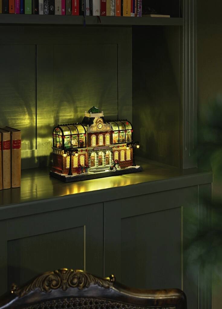 Een miniatuurlamp in de vorm van een historisch gebouw staat verlicht op een donkergroen rek.