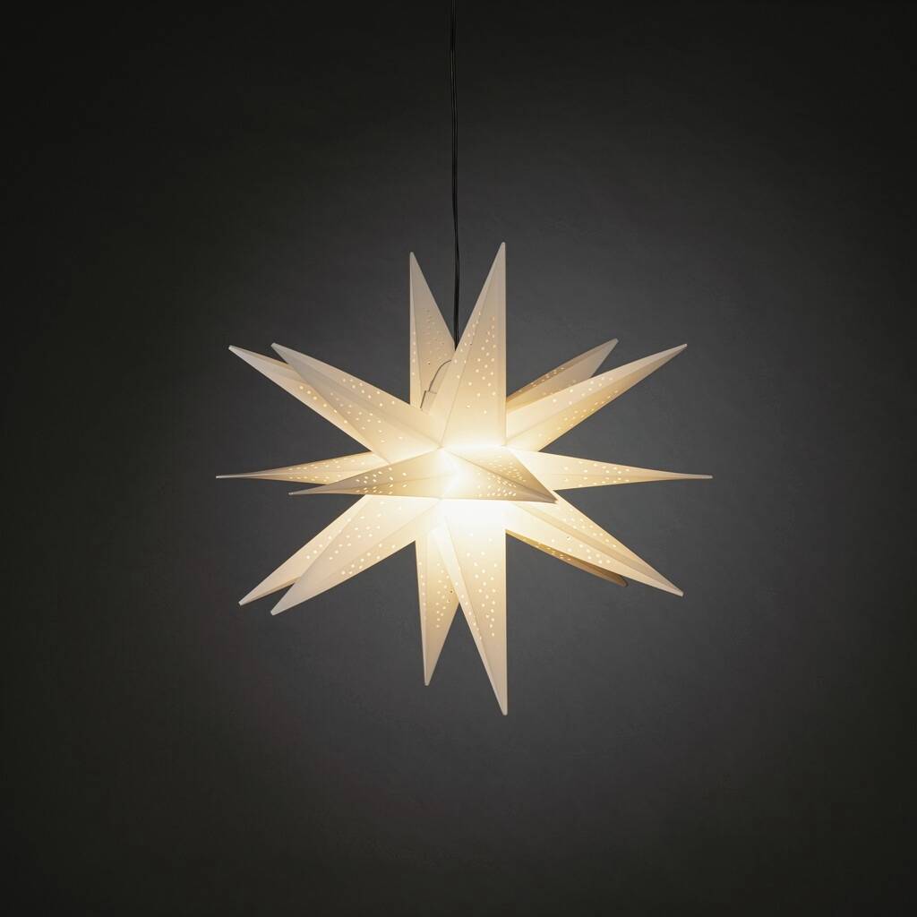 Een verlichte, witte papieren ster met geperforeerde patronen hangt voor een donkere achtergrond en straalt warm licht uit.