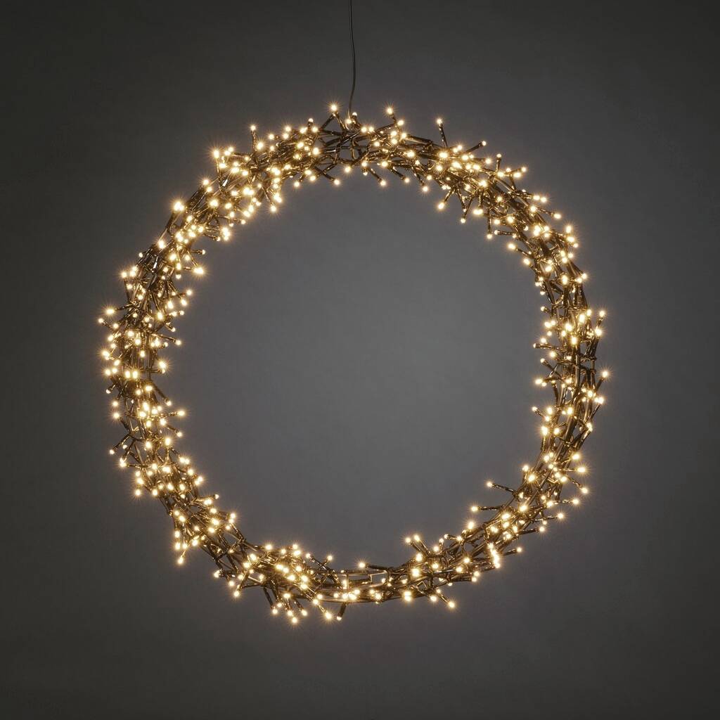 Een stralende, ronde lichtkrans met veel kleine, warmwitte lichtjes hangt voor een neutrale achtergrond.