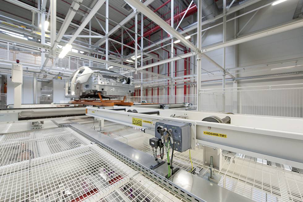 Een auto-carrosserie op een assemblagelijn in een moderne fabriekshall, omgeven door metaalstructuren en technische apparatuur.