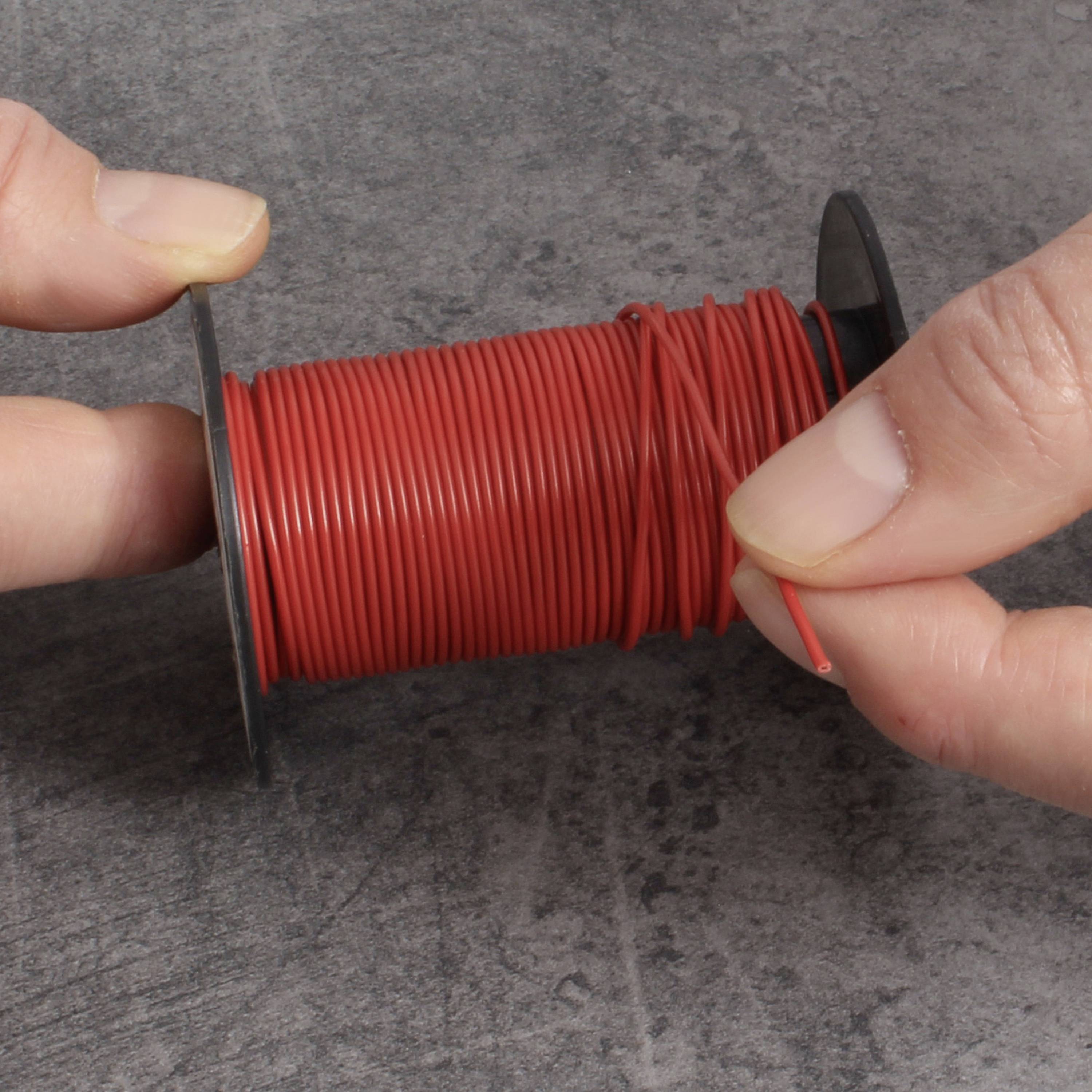 Twee handen houden een rol met rode draad vast. Eén hand trekt het uiteinde, terwijl de andere de spoel vasthoudt. Grijze achtergrond.
