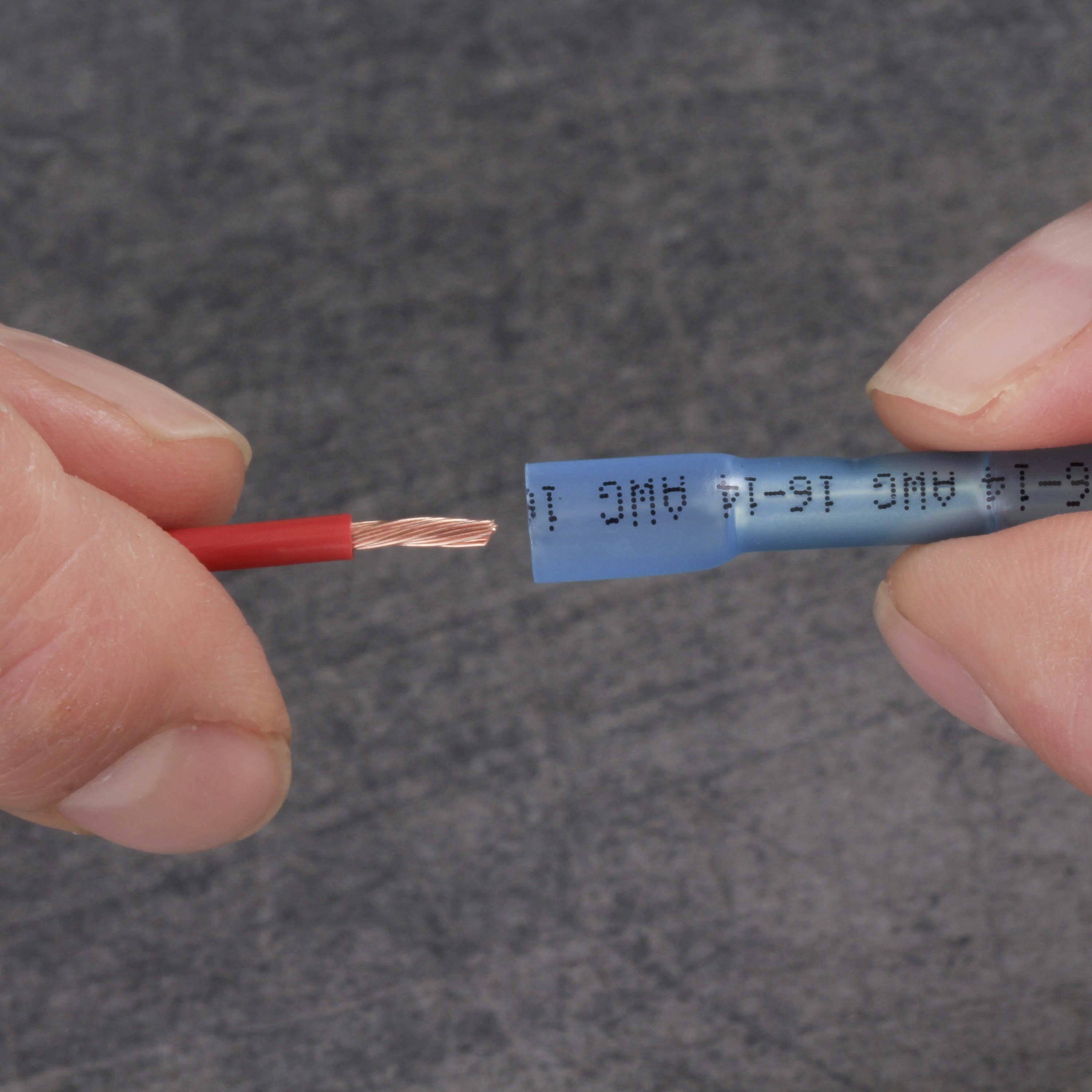 Twee handen houden een rode kabel vast, die in een blauw aansluitelement wordt geschoven. Het uiteinde van de kabel bestaat uit koperen draden.
