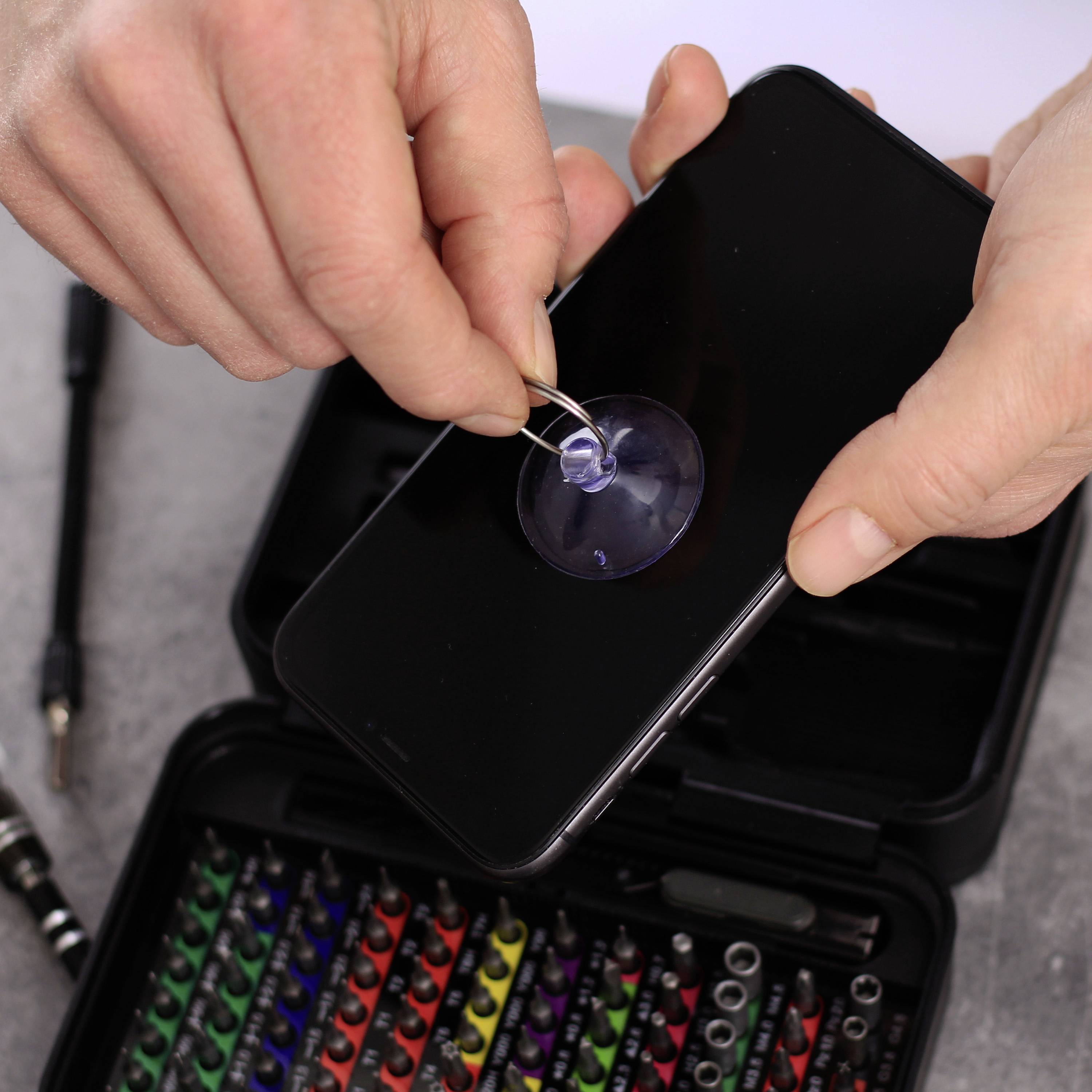 Een persoon repareert een smartphonescherm met een zuignap om het display te verwijderen. Op de achtergrond is een gereedschapskist zichtbaar.