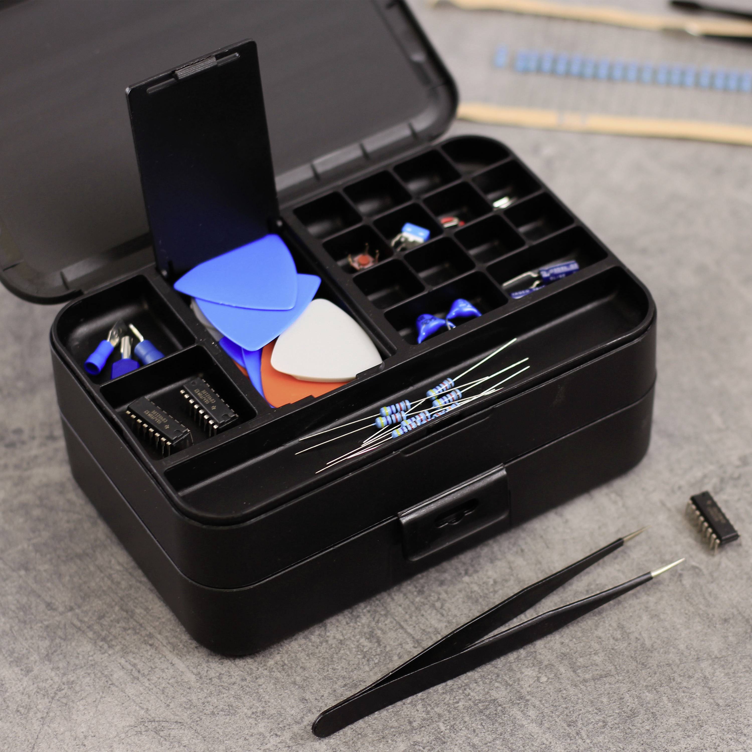 Een geopende gereedschapskist bevat elektronische componenten zoals weerstanden, condensatoren, IC's en pincetten op een tafel.