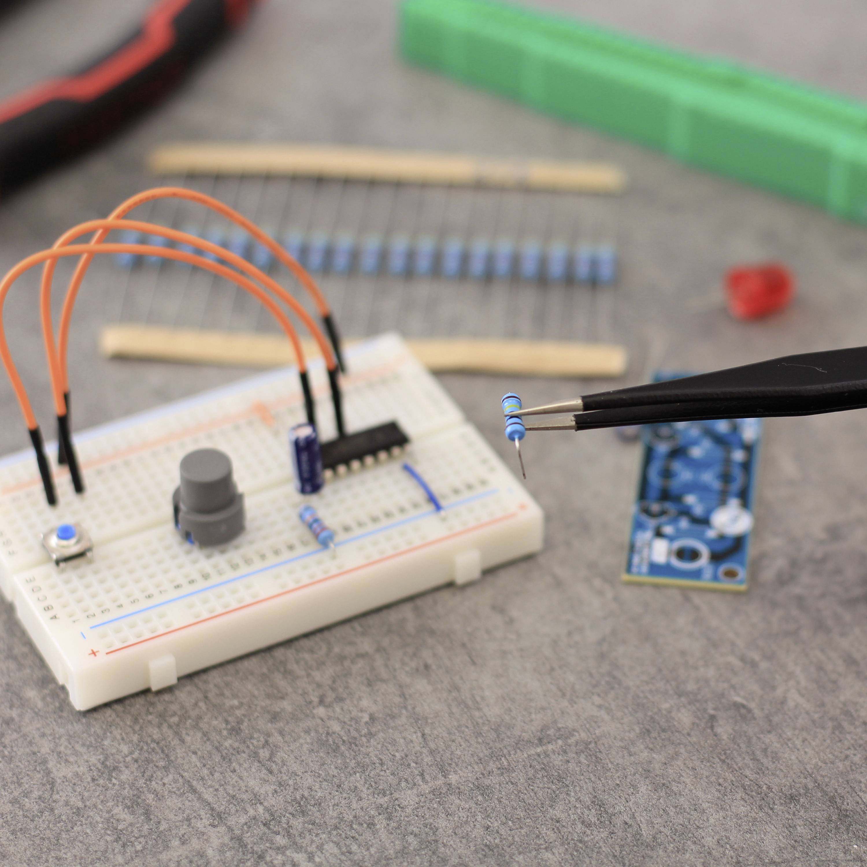 Een breadboard met elektronische componenten zoals een IC, weerstanden en kabels. Een hand houdt een tang vast met een blauw onderdeel.