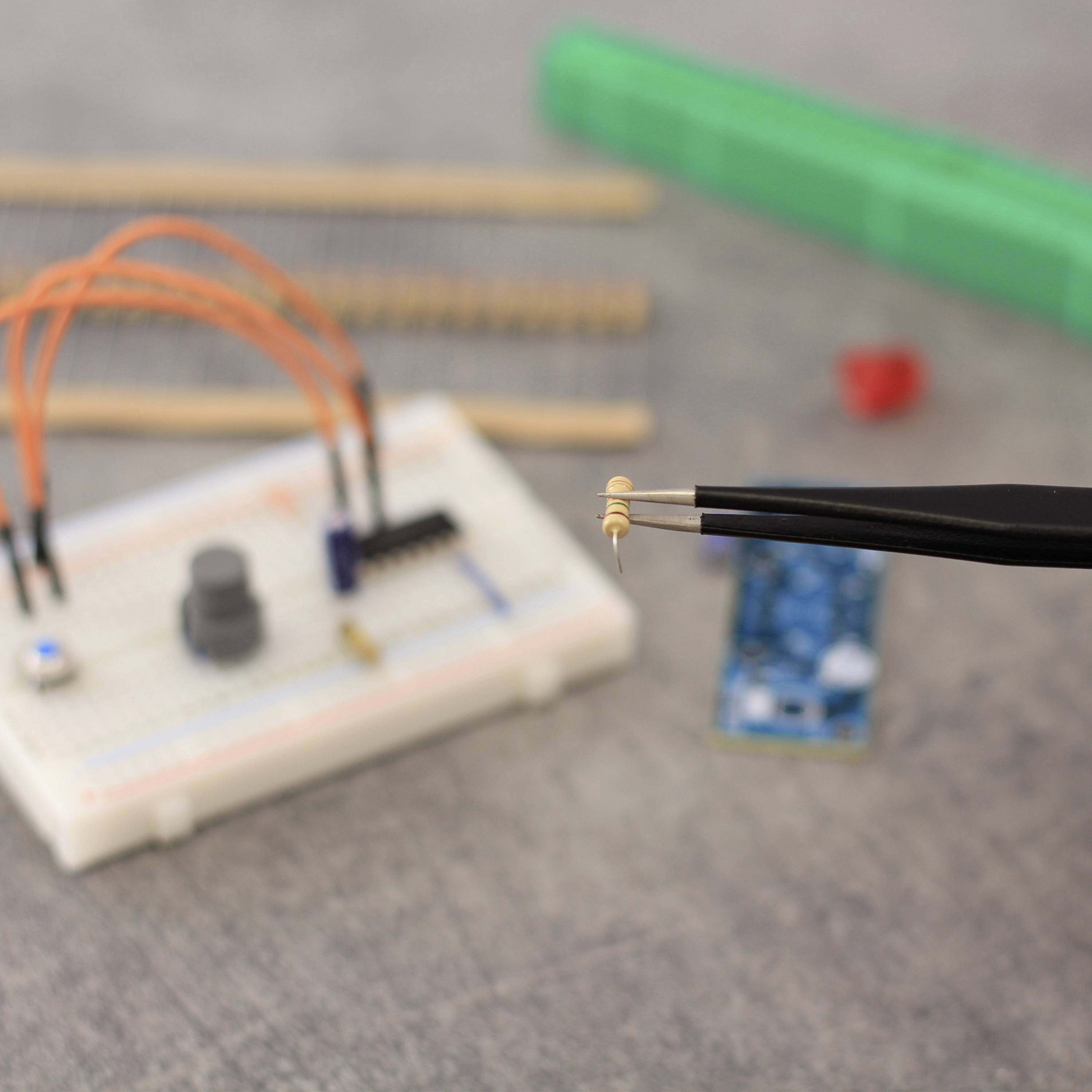 Een close-up van een breadboard met elektronische componenten. Een hand houdt met een pincet een kleine weerstand vast.