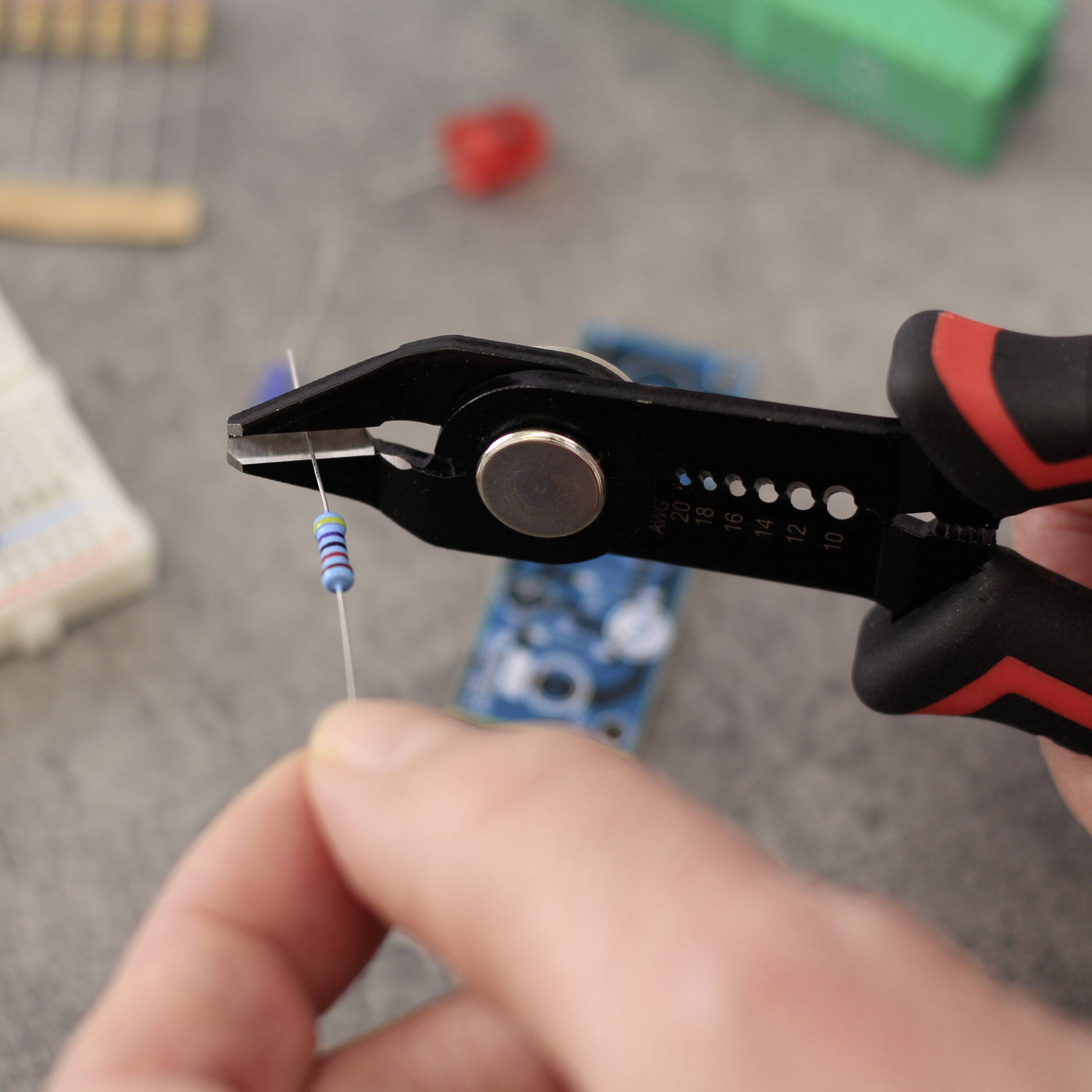 Een hand houdt met een tang een weerstand vast boven een werkoppervlak met elektronische componenten.