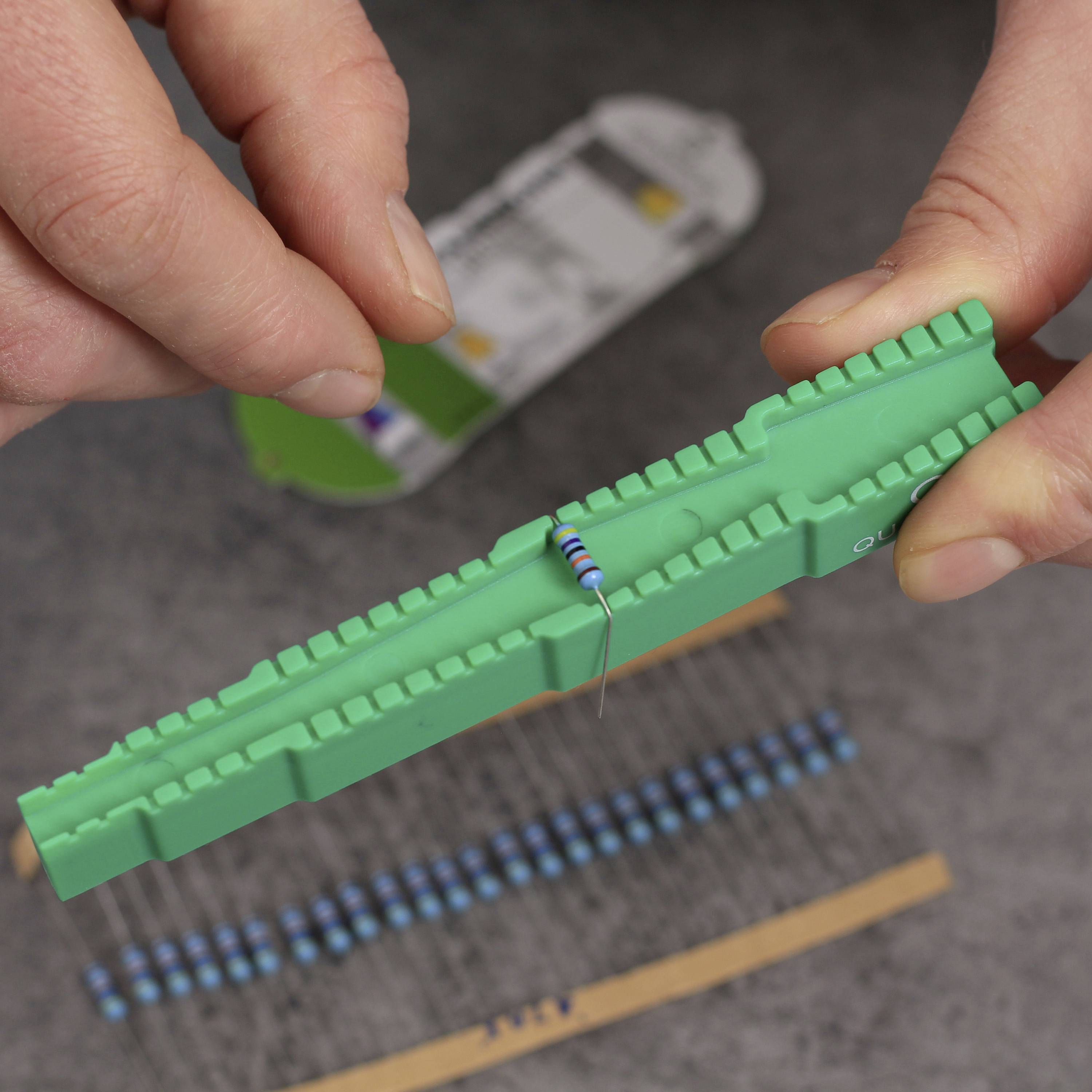 Twee handen monteren een weerstand op een groen breadboard. Achtergrond onscherp. Focus op elektronisch werkproces.