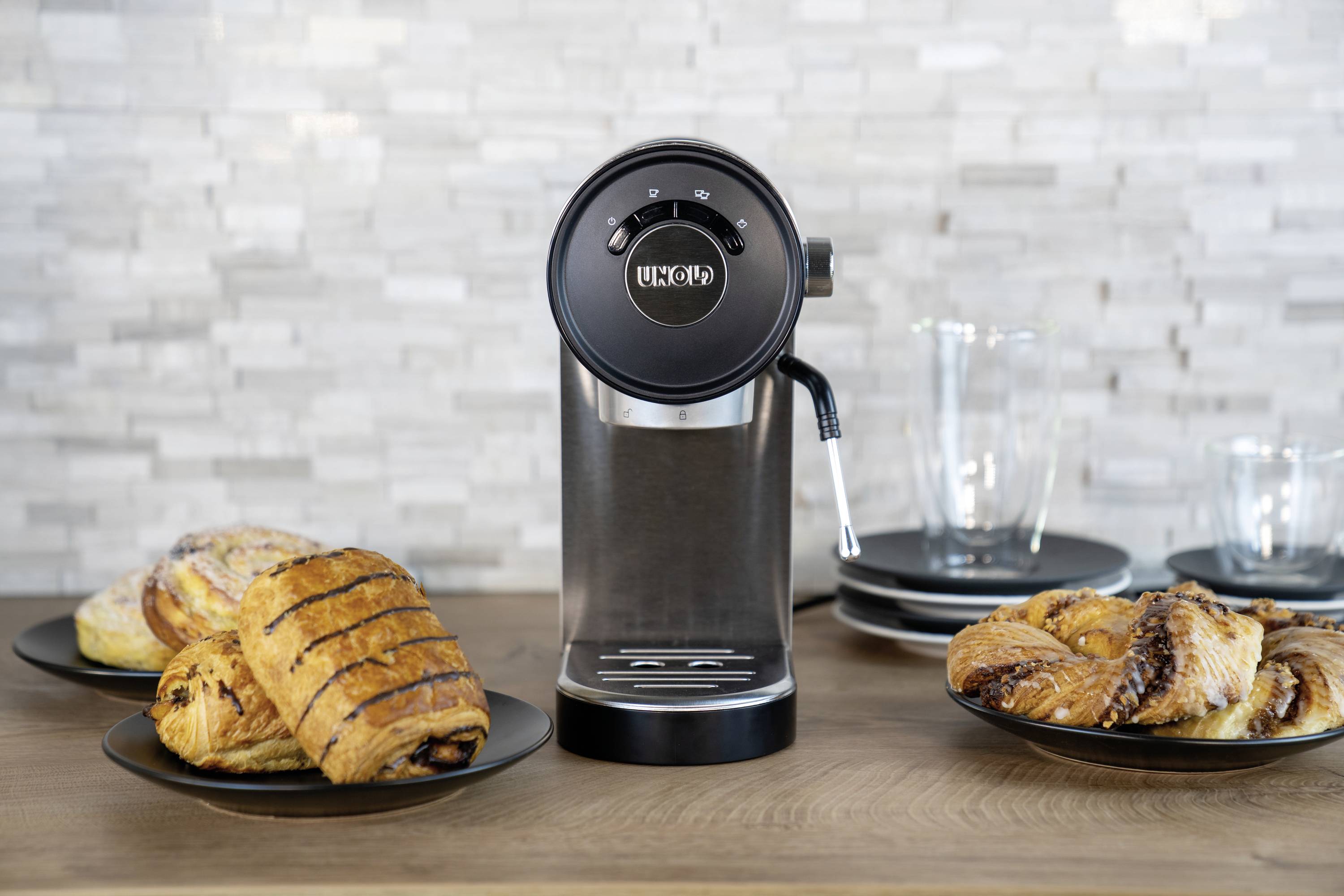Een zwarte koffiemachine staat op een houten tafel, omringd door borden met vers gebakken croissants en gebak.