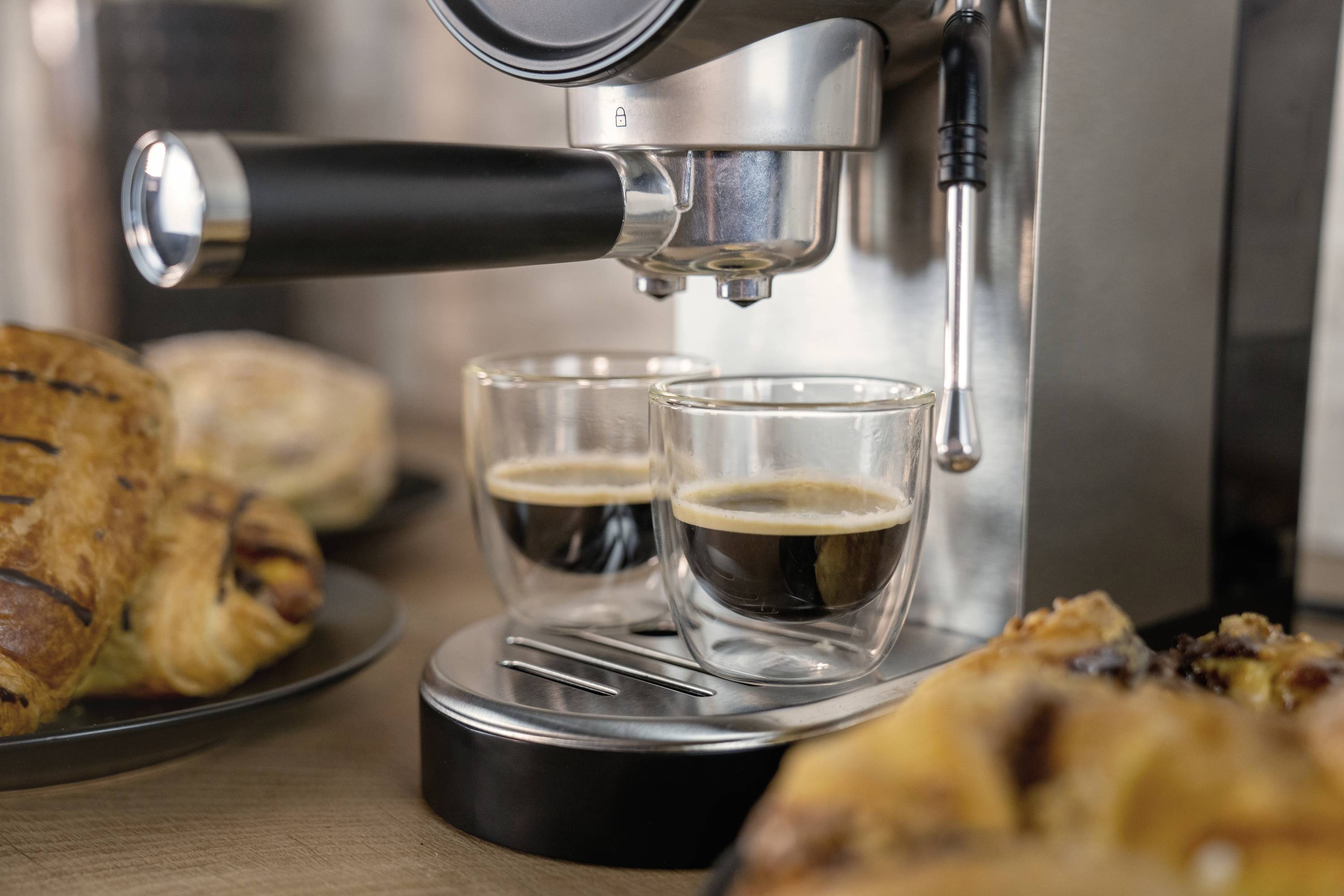 Espressomachine zet twee kopjes koffie, omringd door gebak.