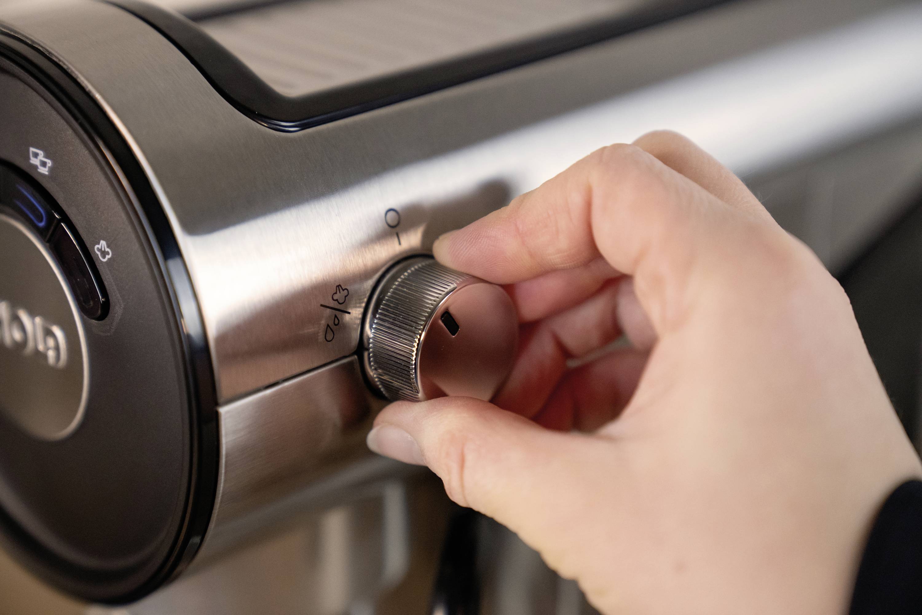 Een hand draait de knop van een koffiemachine om de maalgraad in te stellen.