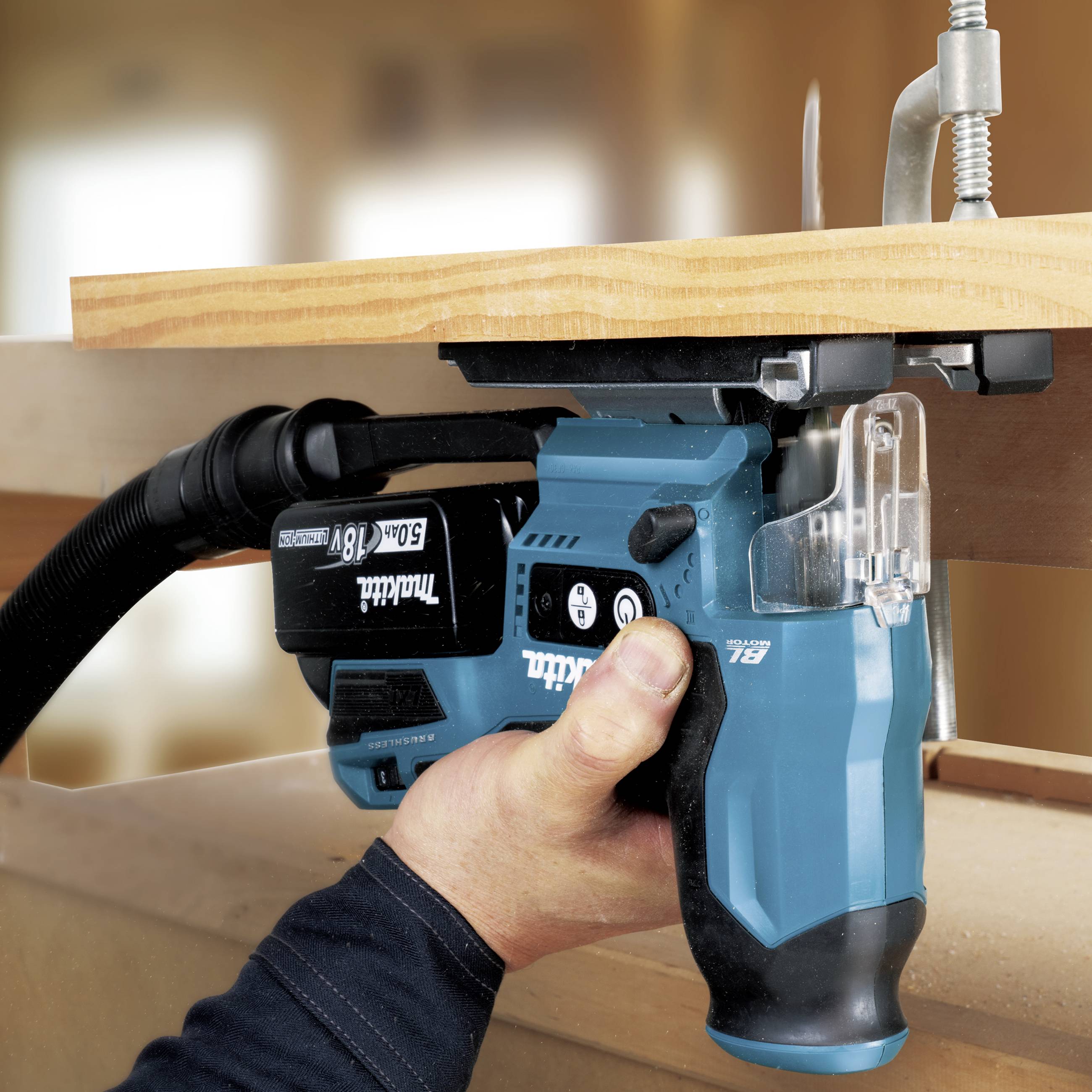 Een blauwe accusaw snijdt door een houten plank. Een hand bestuurt de zaag. Een lijmklem houdt de plank stabiel.