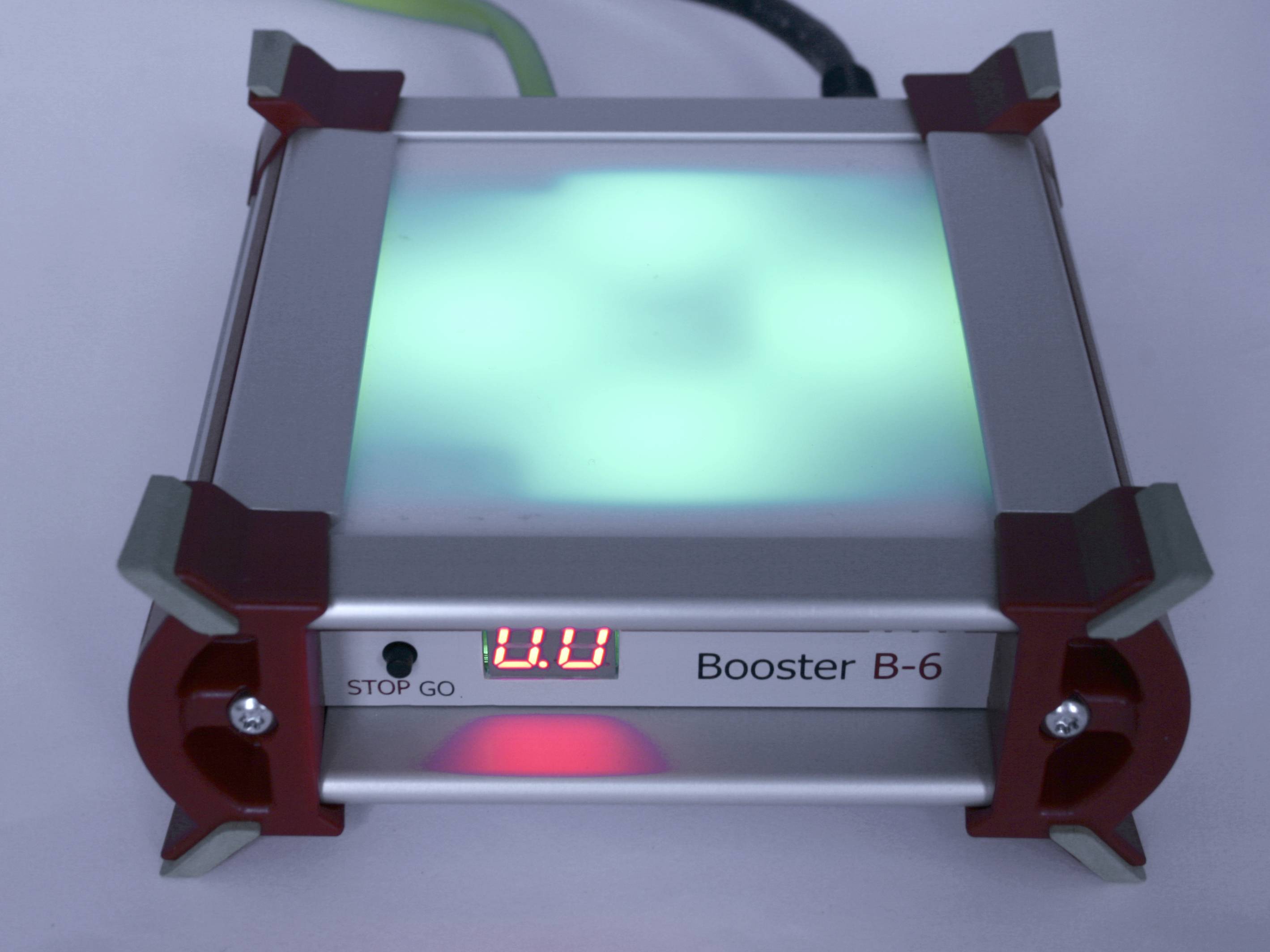 Een vierkante apparaat met het opschrift 'Booster B-6'. Een digitaal display toont '0.0'. Een fel groen licht is zichtbaar.