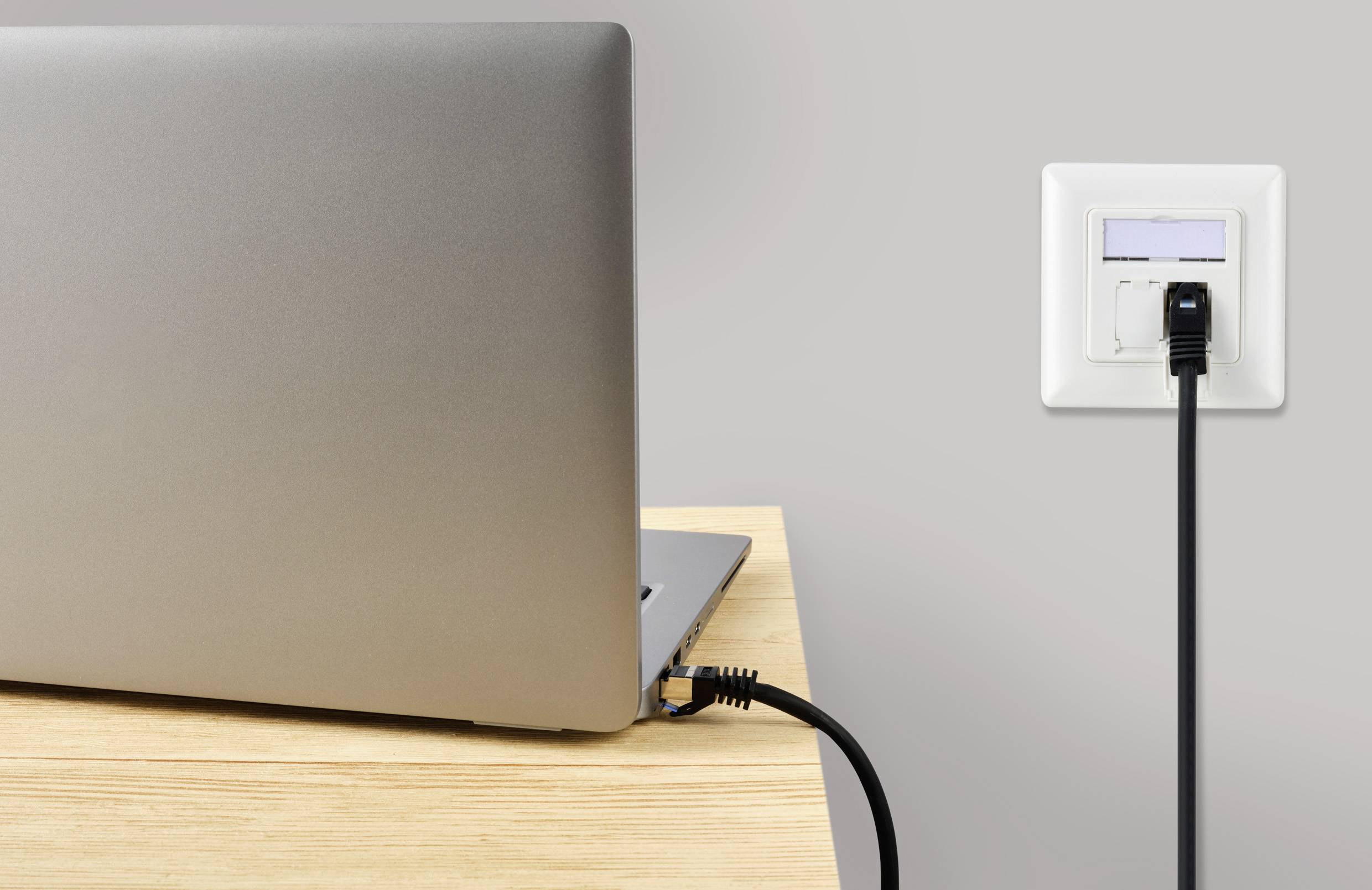 Een laptop op een tafel is met een netwerkkabel aangesloten op een wandcontactdoos.