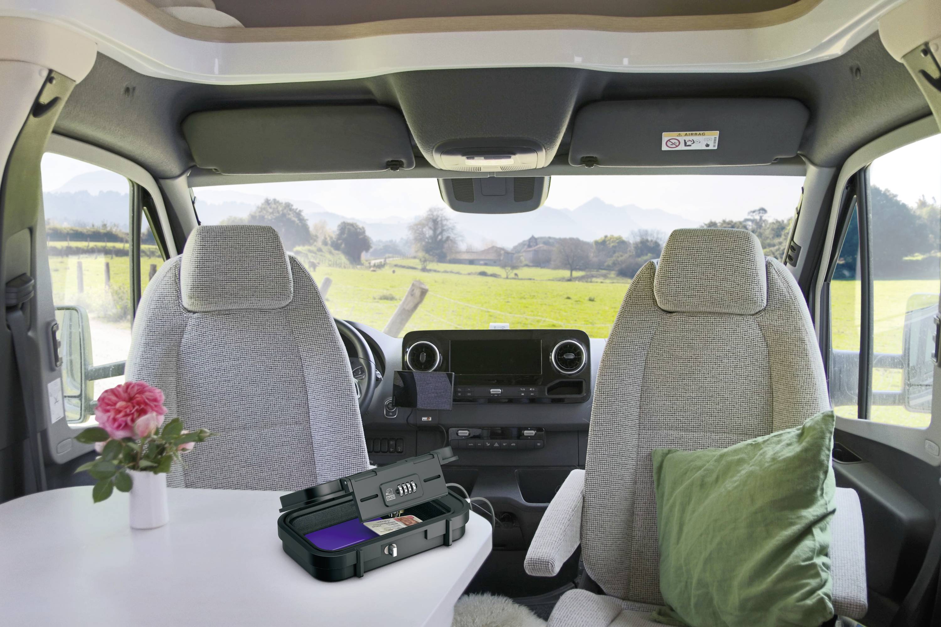 Interieur van een camper met twee voorzetels, een tafel met een bloem en een groen kussen. Uitzicht naar buiten op het landschap.