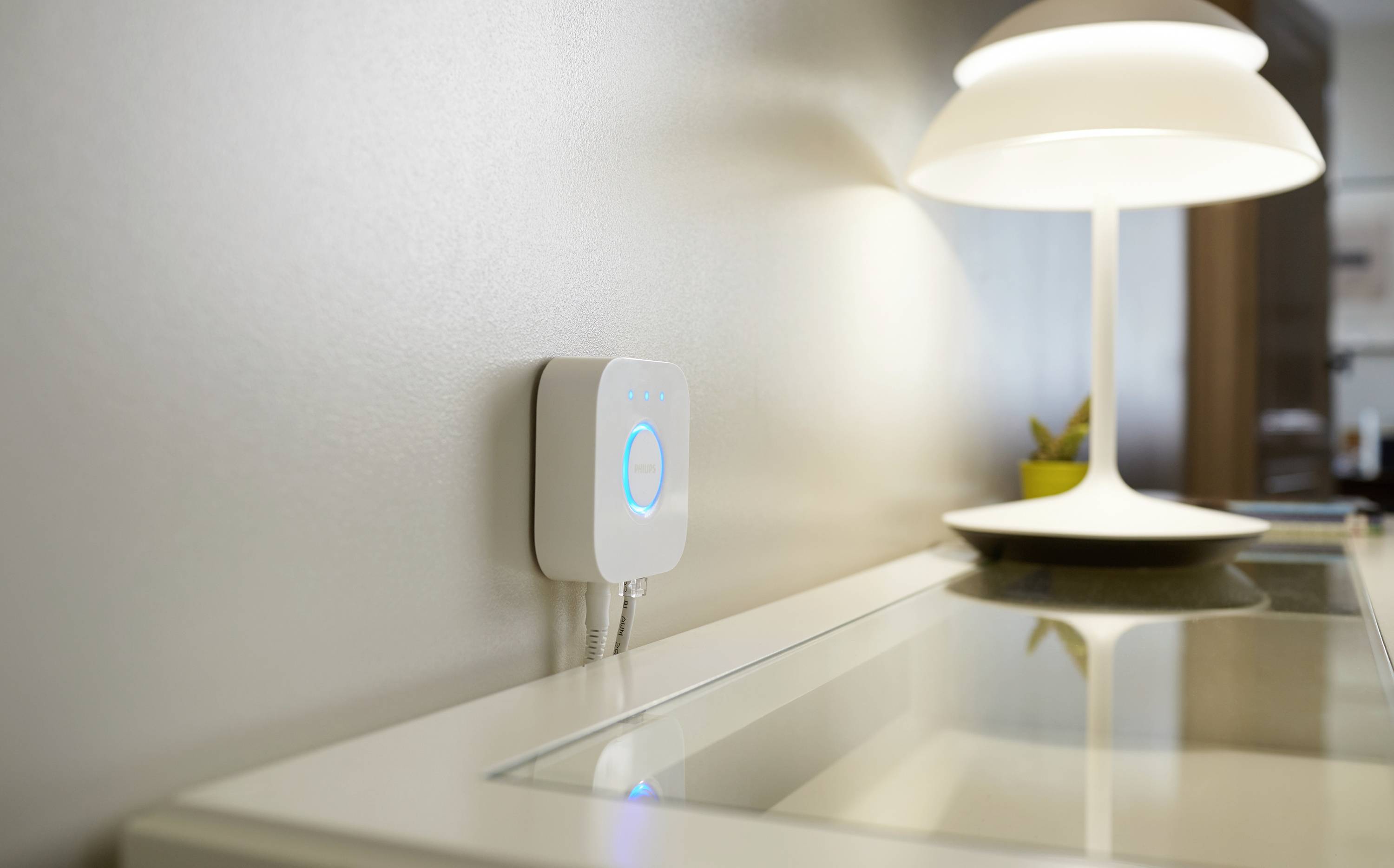 Een witte wifi-router schijnt blauw en is aan de muur bevestigd naast een witte tafel met lamp. De scène oogt modern.