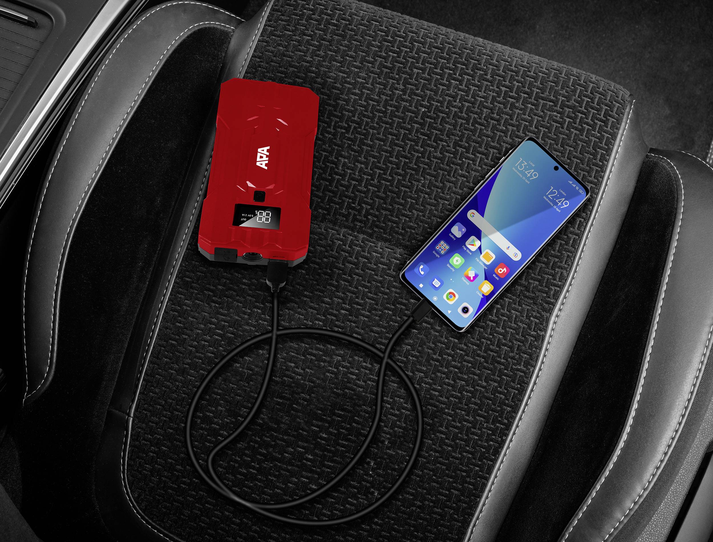 Een rood oplaadapparaat met digitale weergave ligt op een autostoel en is verbonden met een smartphone.