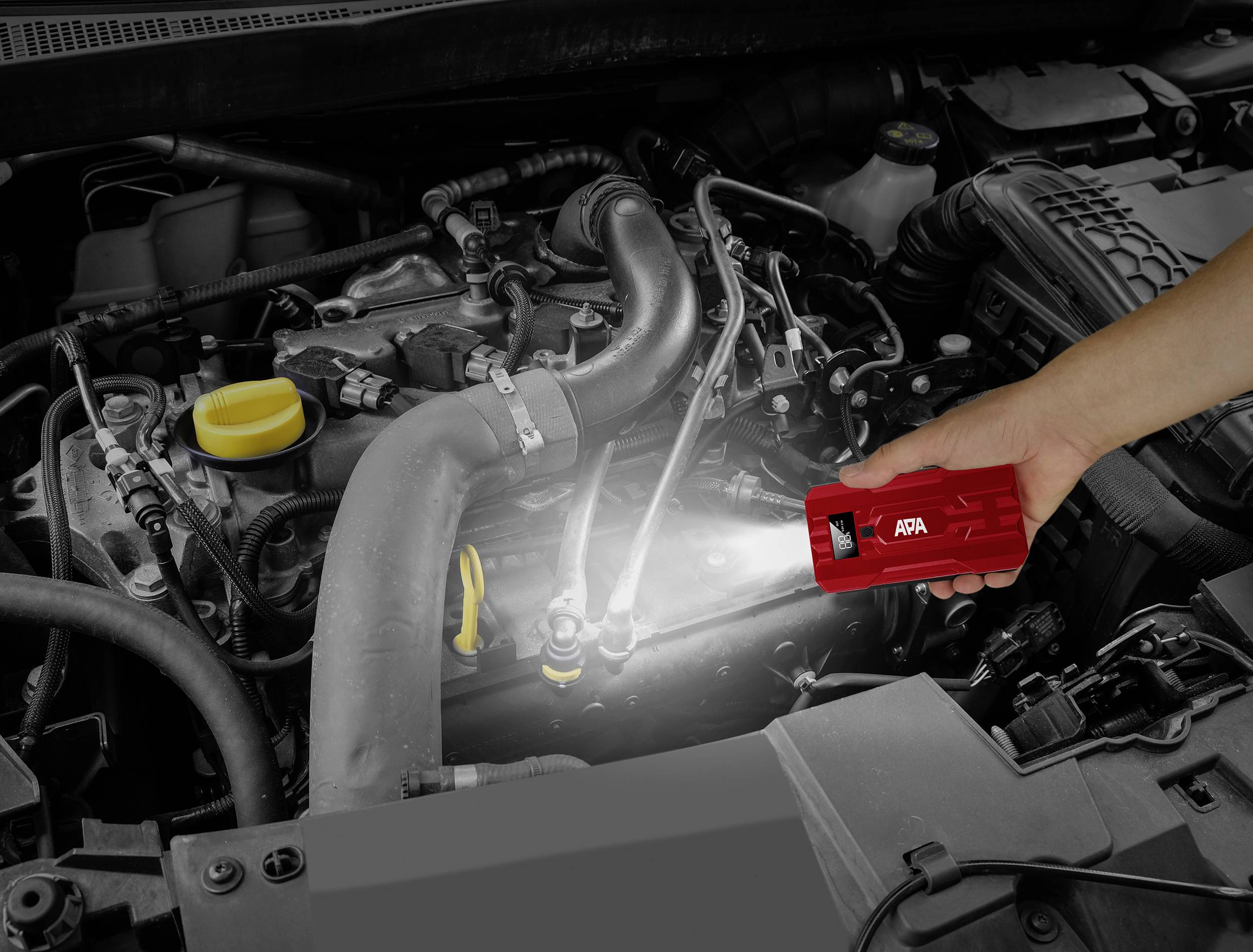 Een hand houdt een rode zaklamp met het opschrift 'APA' die de motorruimte van een auto verlicht.