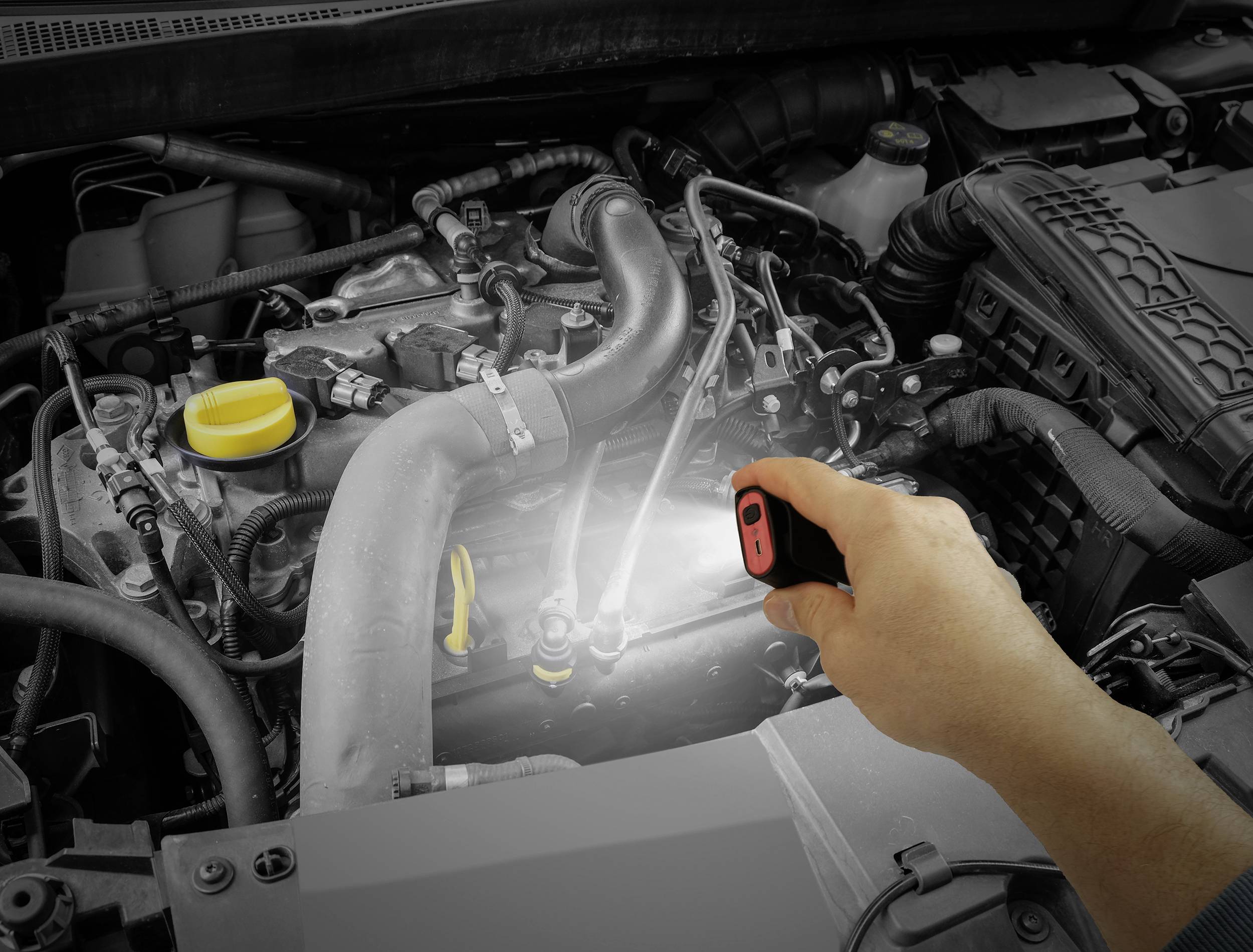Een persoon schijnt met een zaklamp op de motor van een auto om de details van de motorcomponenten te bekijken.