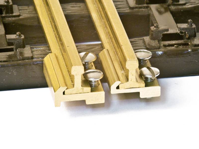 Close-up van twee parallel lopende modeltreinrails, vastgeschroefd op een zwarte houten ondergrond.